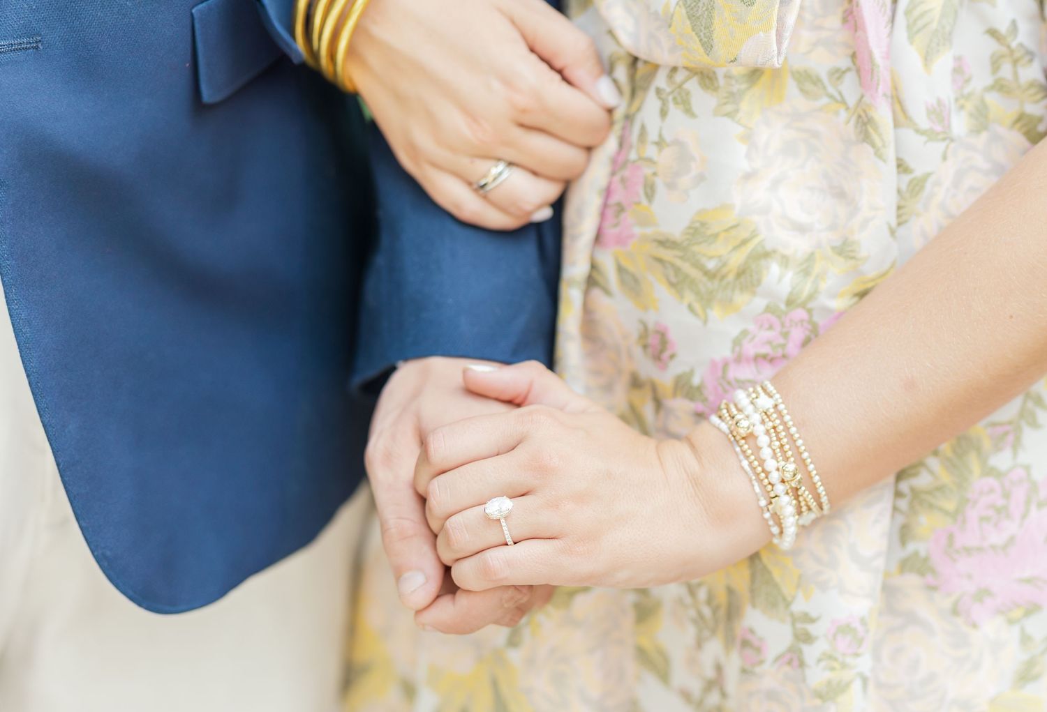 Close-up detail of hands showing wedding rings against a floral patterned dress.