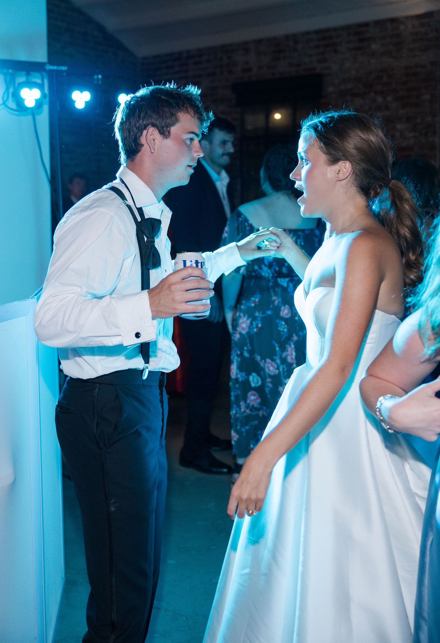 Bride and groom share a playful moment on the dance floor under blue reception lighting at their wedding.