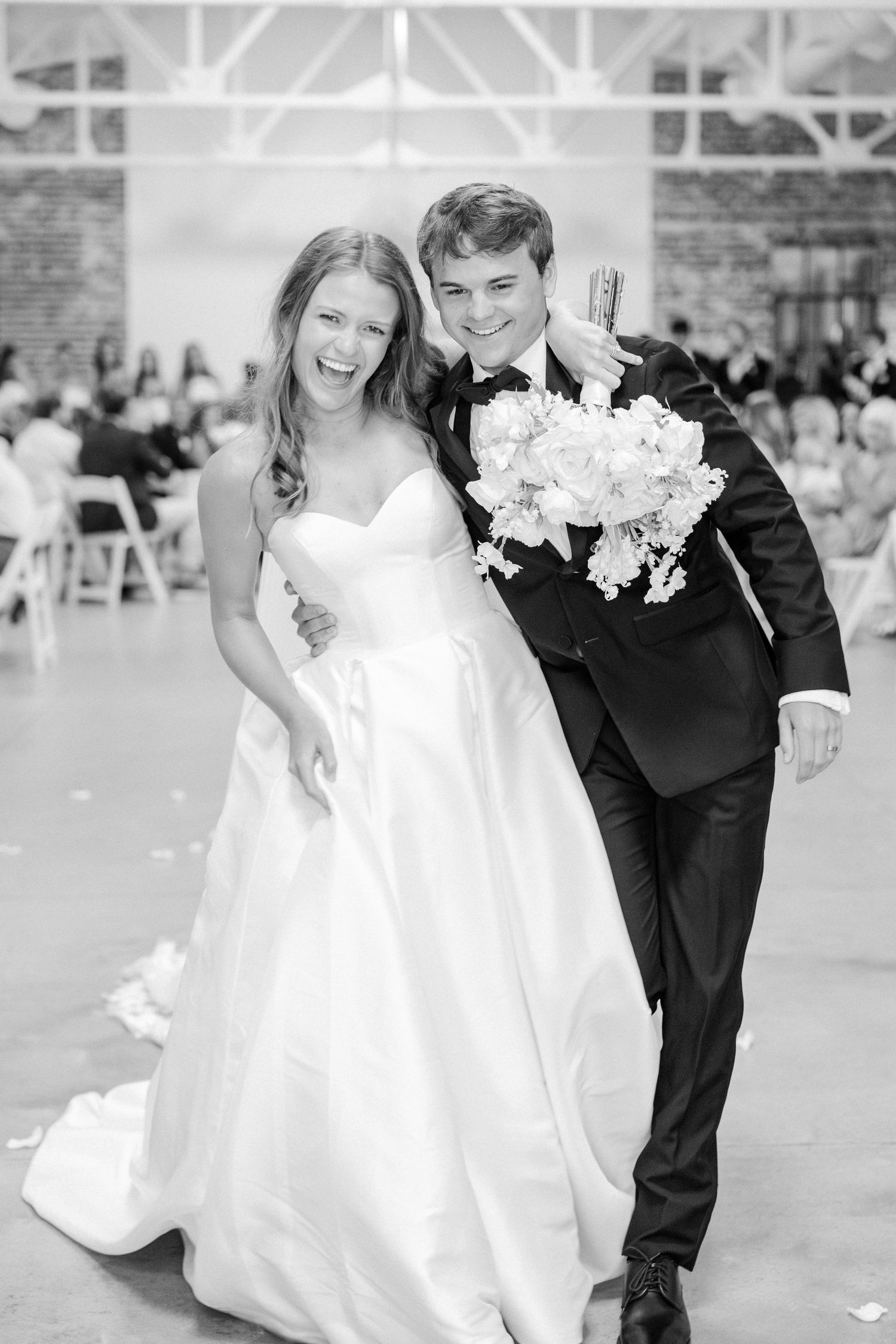 Bride and groom laugh joyfully while walking down the aisle after their wedding ceremony in black and white photo.