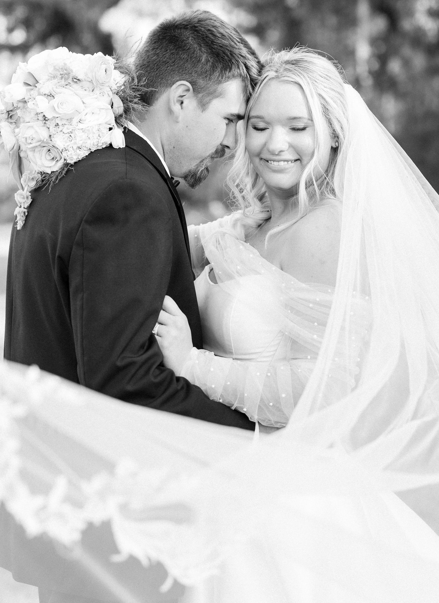 Black and white photo of bride and groom sharing an intimate moment under flowing veil.