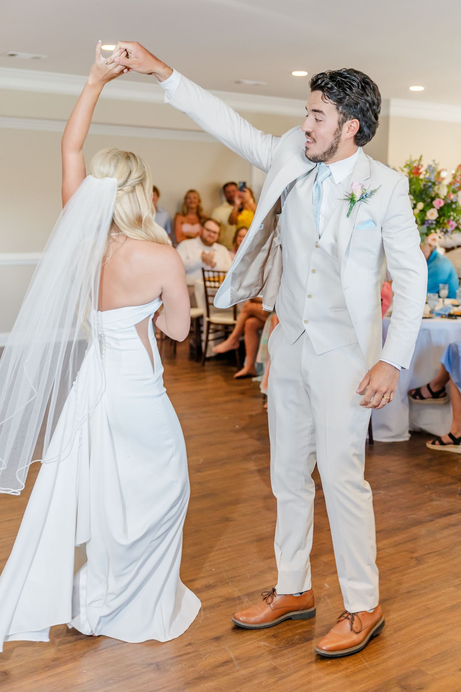 Bride and groom share first dance, groom twirling bride in white gown and veil at wedding reception.