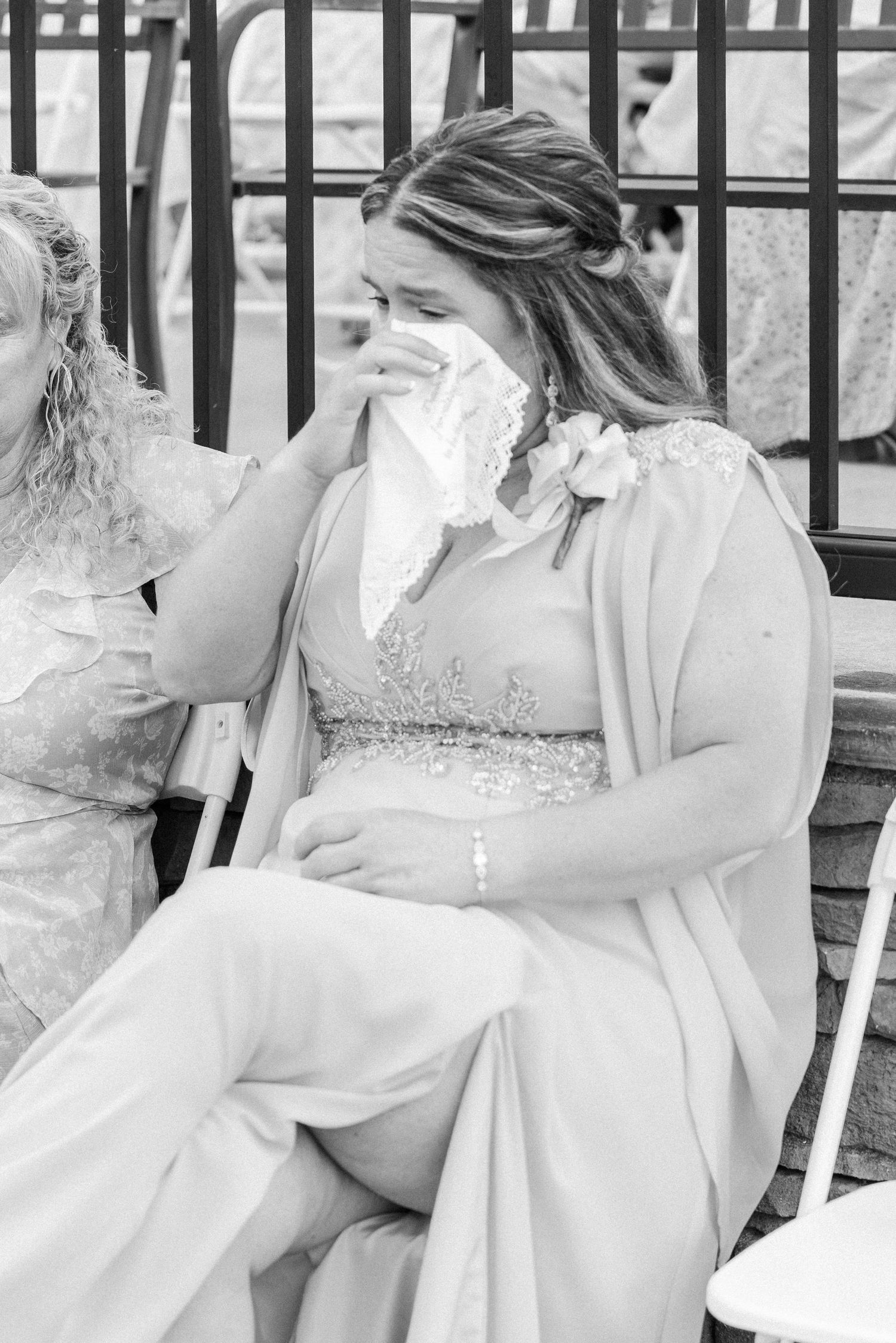 Emotional wedding guest wipes tears with handkerchief during outdoor wedding ceremony in black and white.