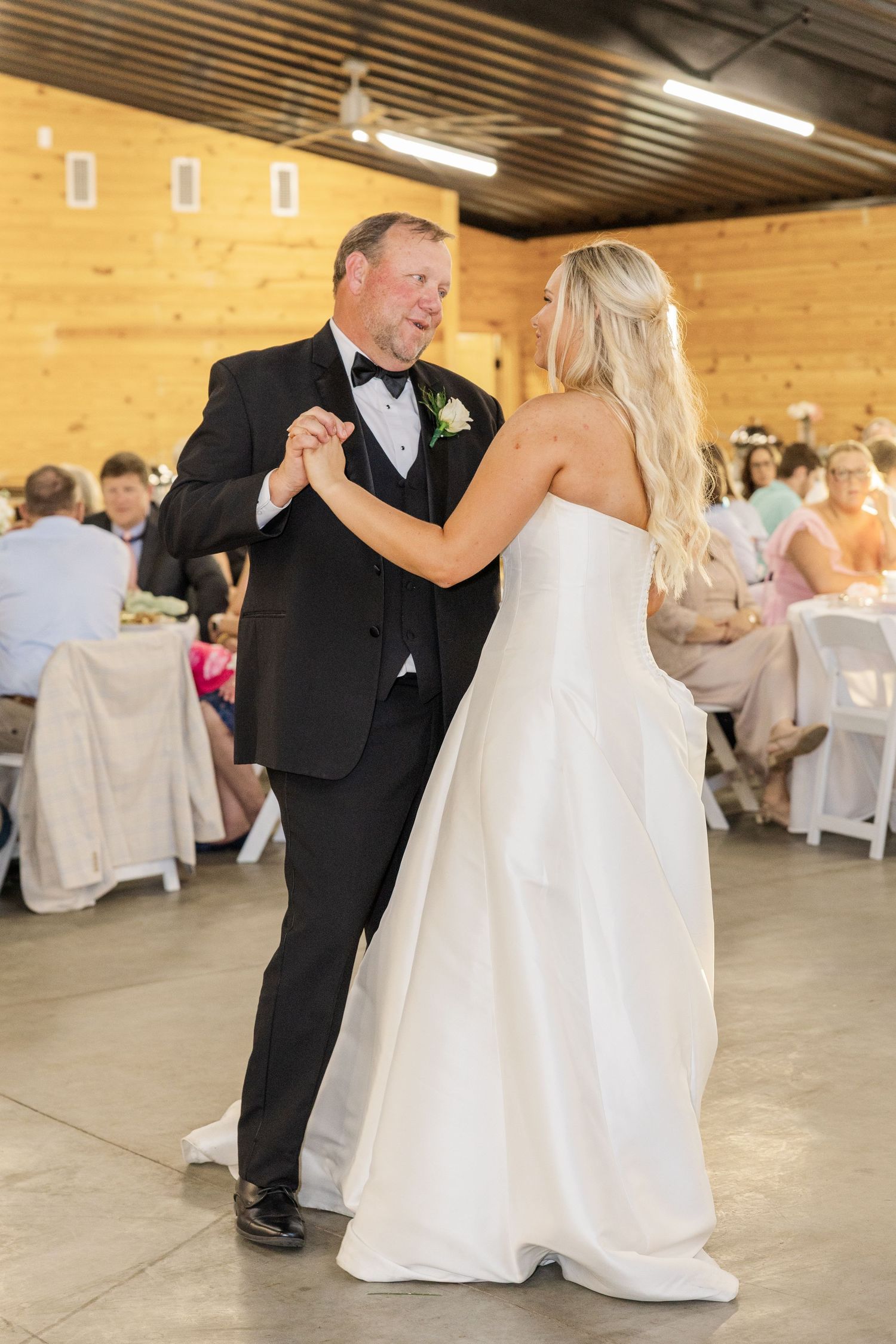 Bride in white strapless gown shares father-daughter dance at rustic barn wedding reception.