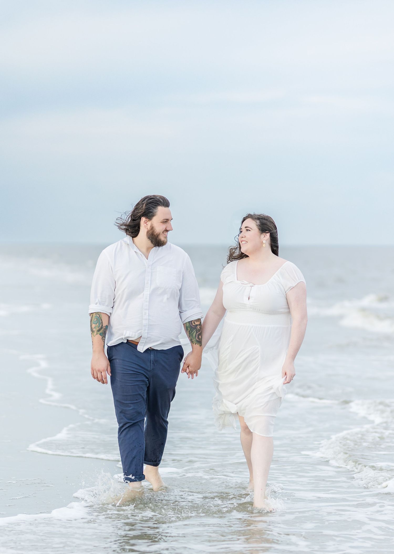 Couple wading in ocean waves during a romantic beach photoshoot.