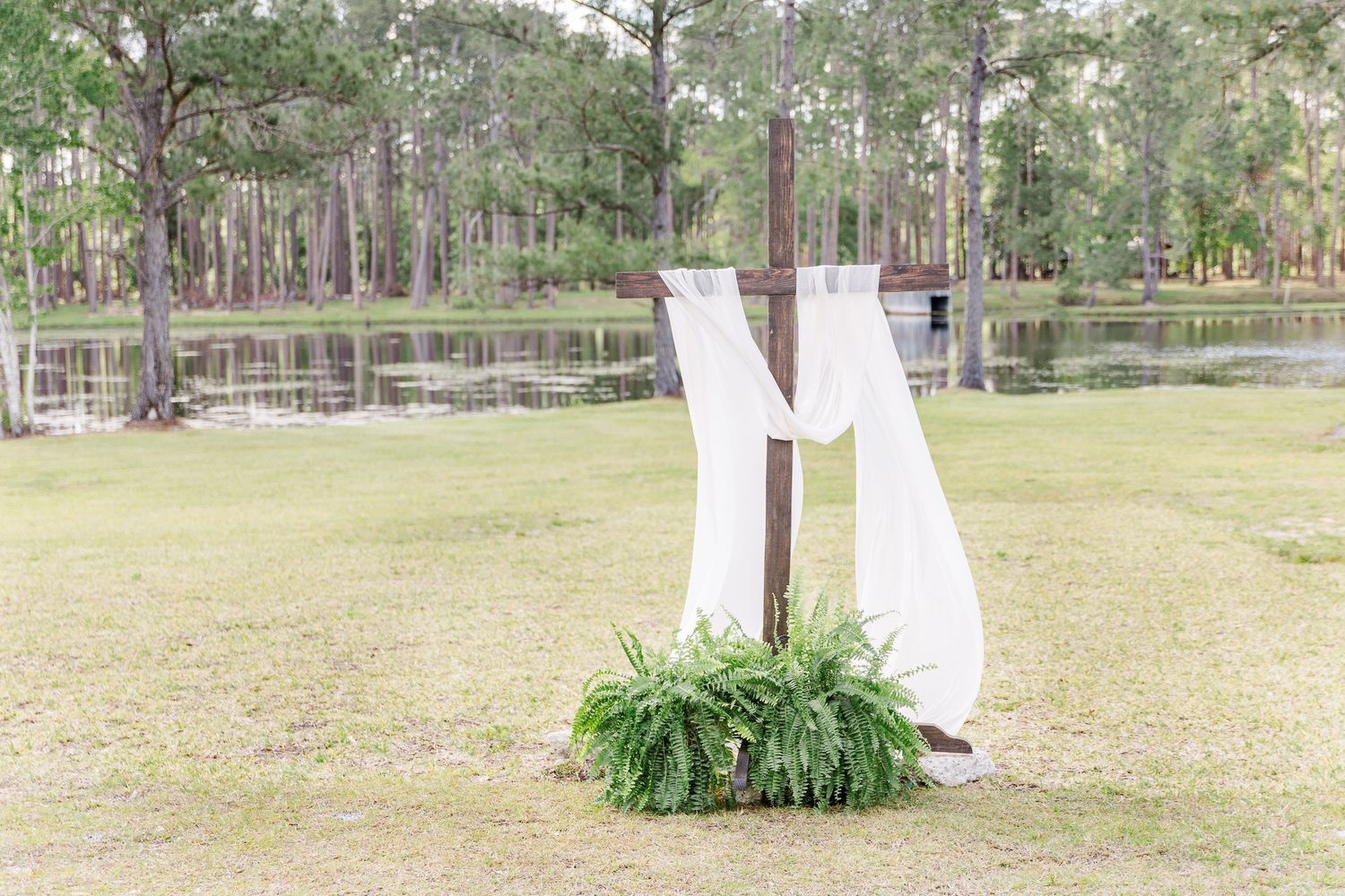 White wedding dress hanging outdoors between trees with greenery at the base.