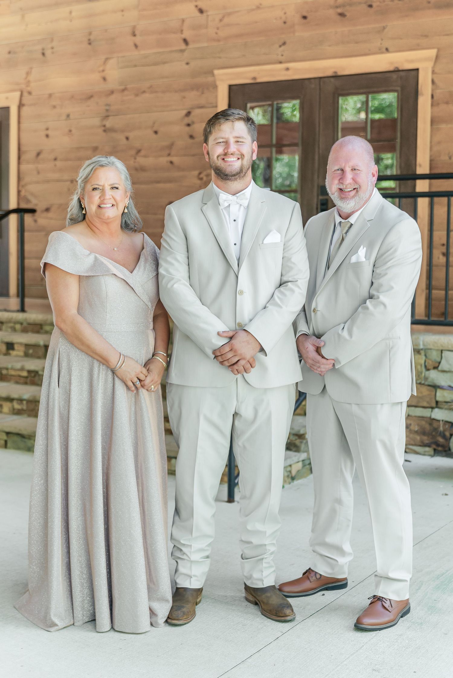 Three people in formal attire pose together at a rustic venue.