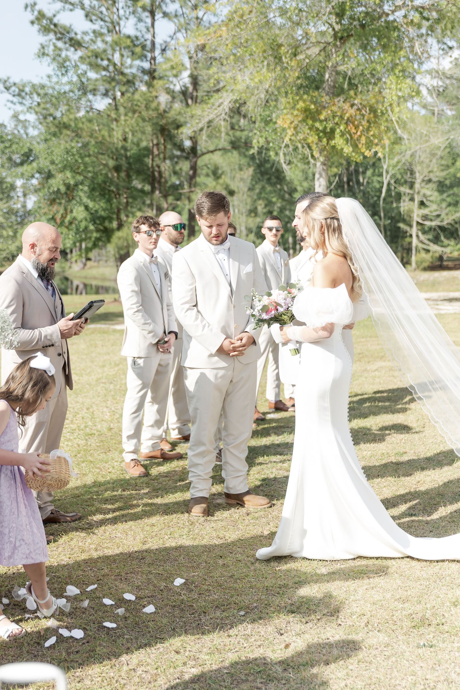 Outdoor wedding ceremony with wedding party in light colored suits and flowing white dress.