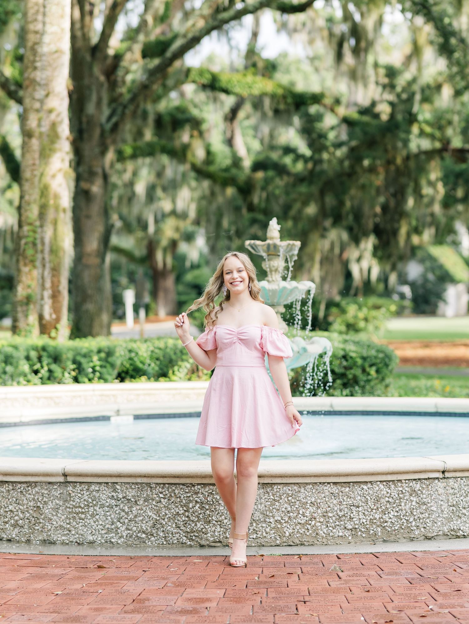 Cheerful child in a pink dress twirls and dances around a fountain in a lush garden setting.
