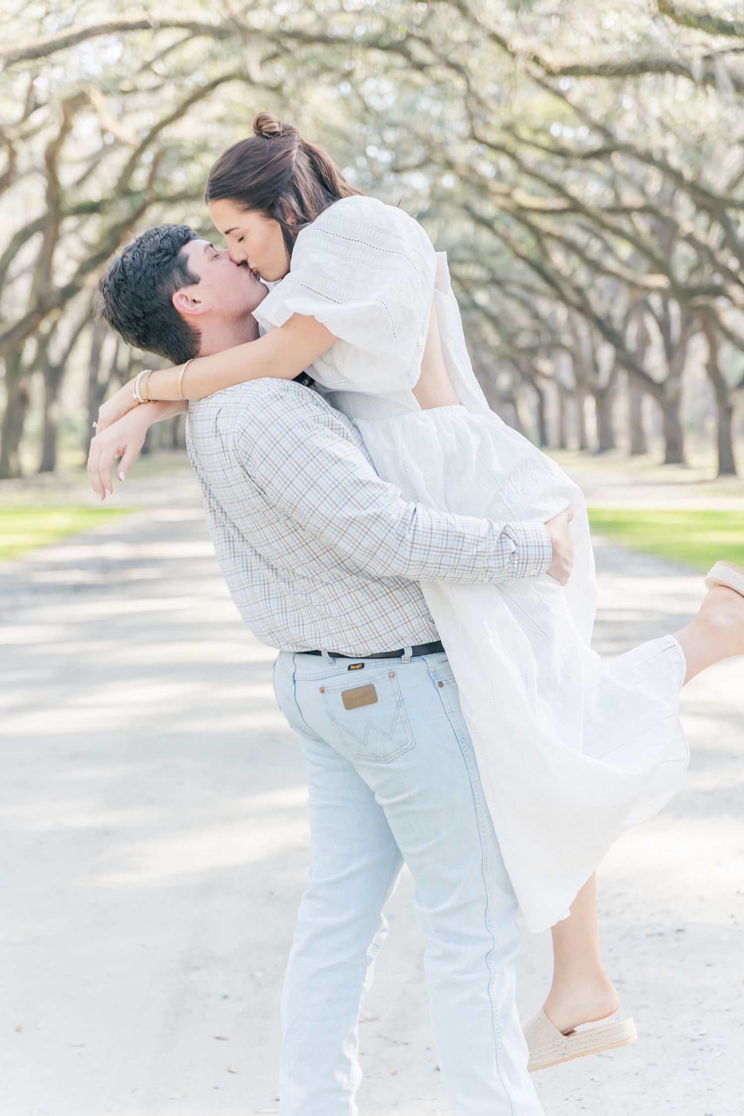 An intimate embrace captured in soft lighting under a natural arch of oak trees.