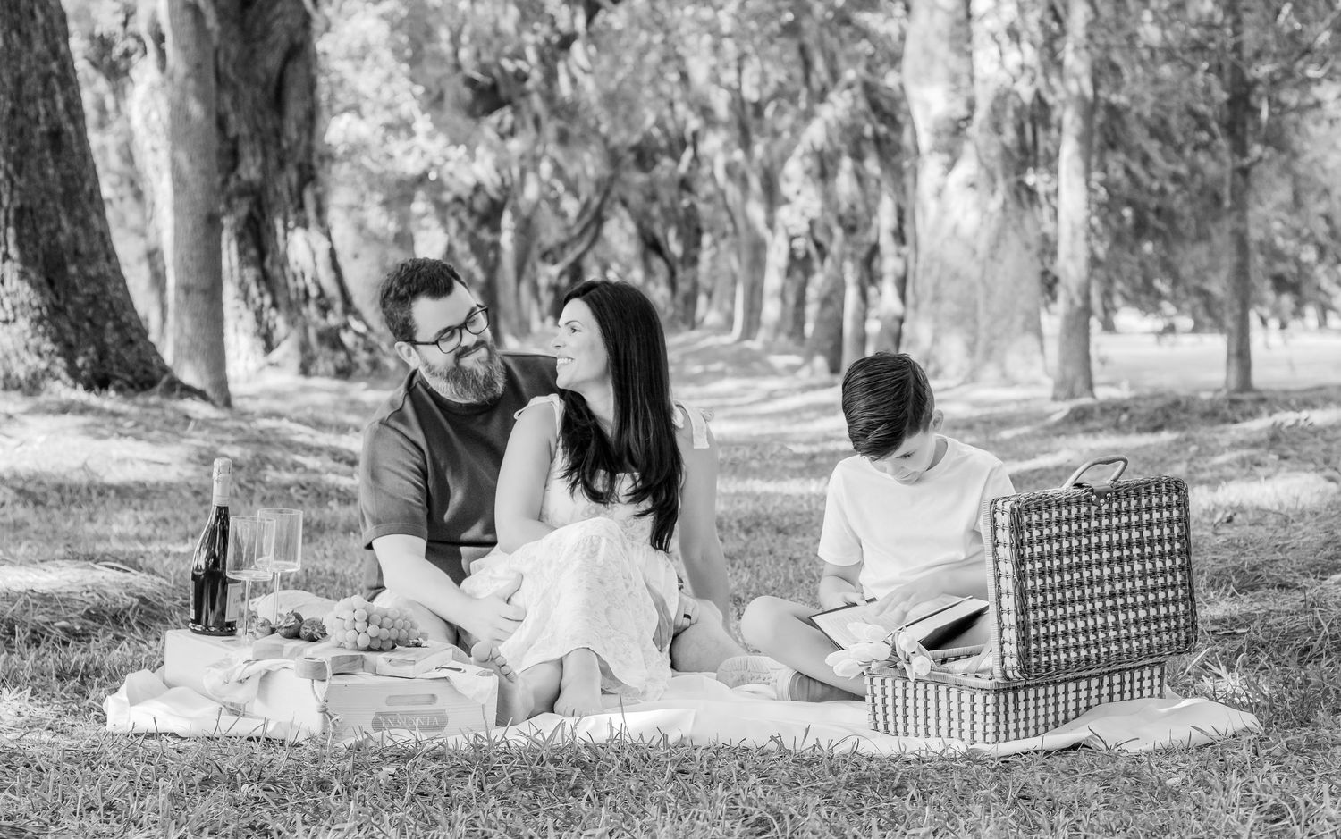 Three people relax on a picnic blanket under Spanish moss-draped trees in black and white.