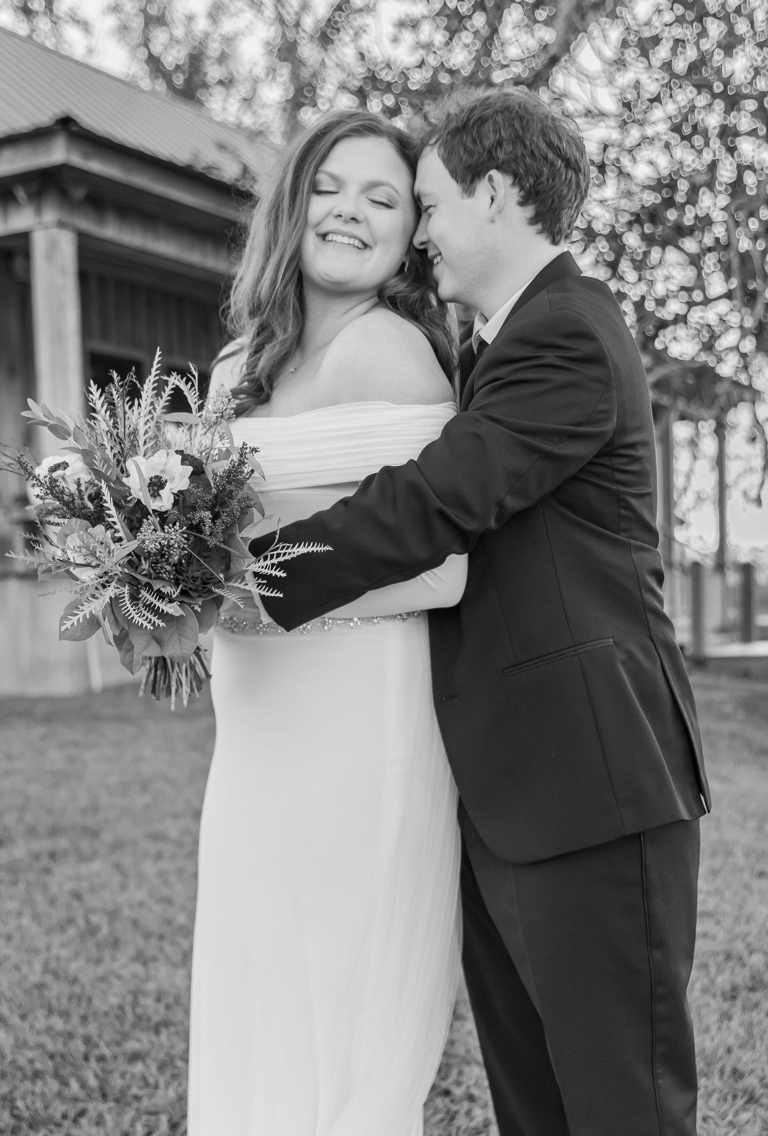 A joyful wedding moment captured in black and white with the couple embracing while holding a floral bouquet.