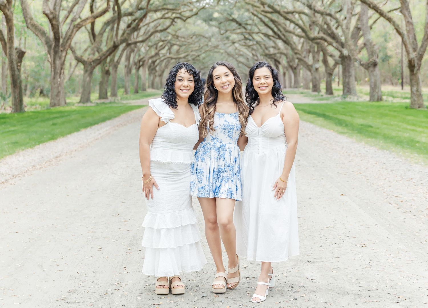 Group photo of three women in coordinating white and blue dresses on a scenic pathway.