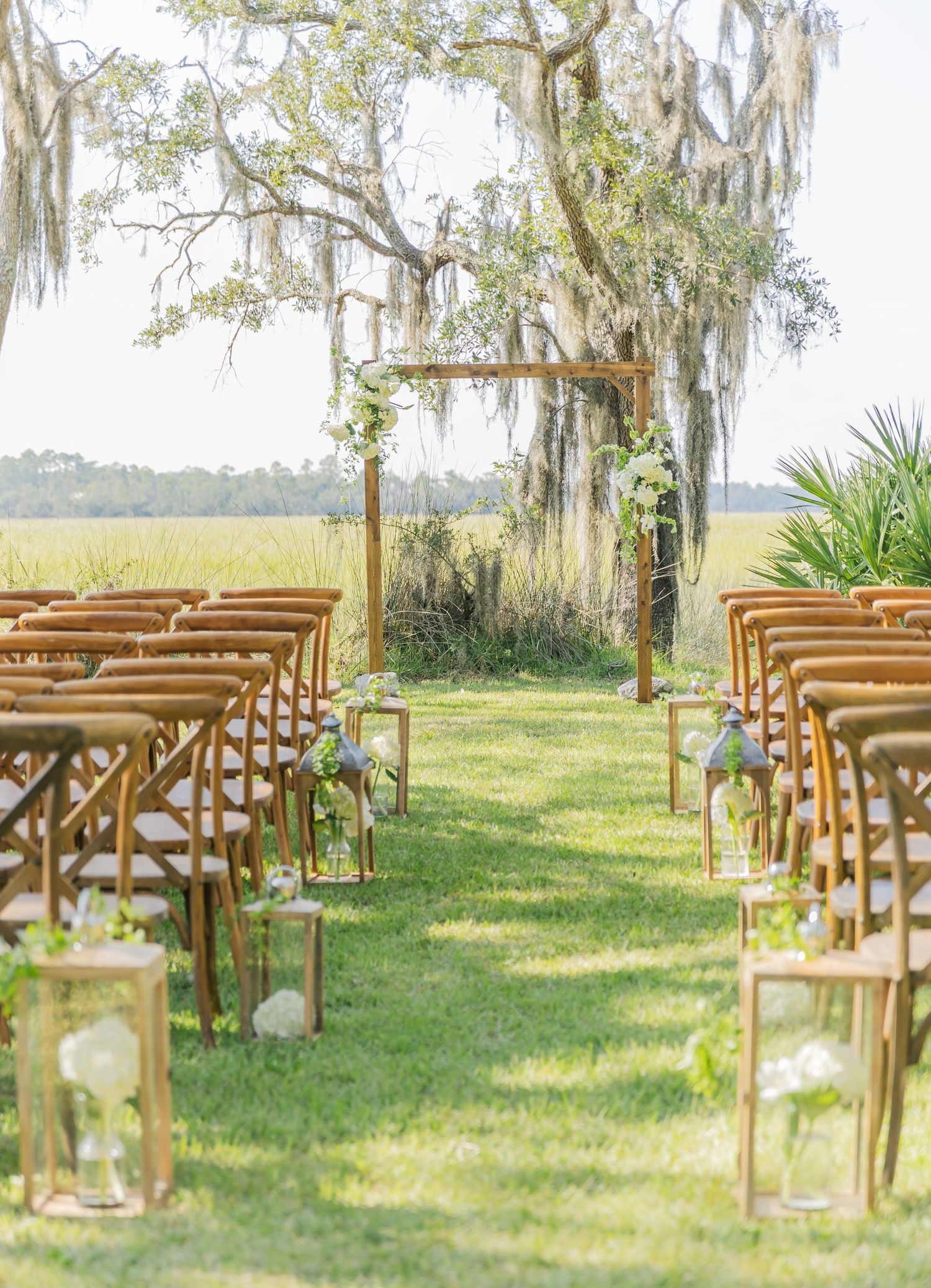 Elegant outdoor wedding aisle with wooden chairs and a simple wooden arch decorated with greenery.