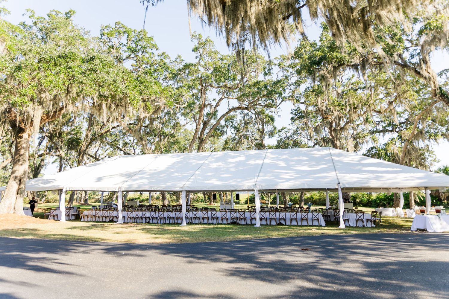 White event tents set up under large oak trees for an outdoor gathering.