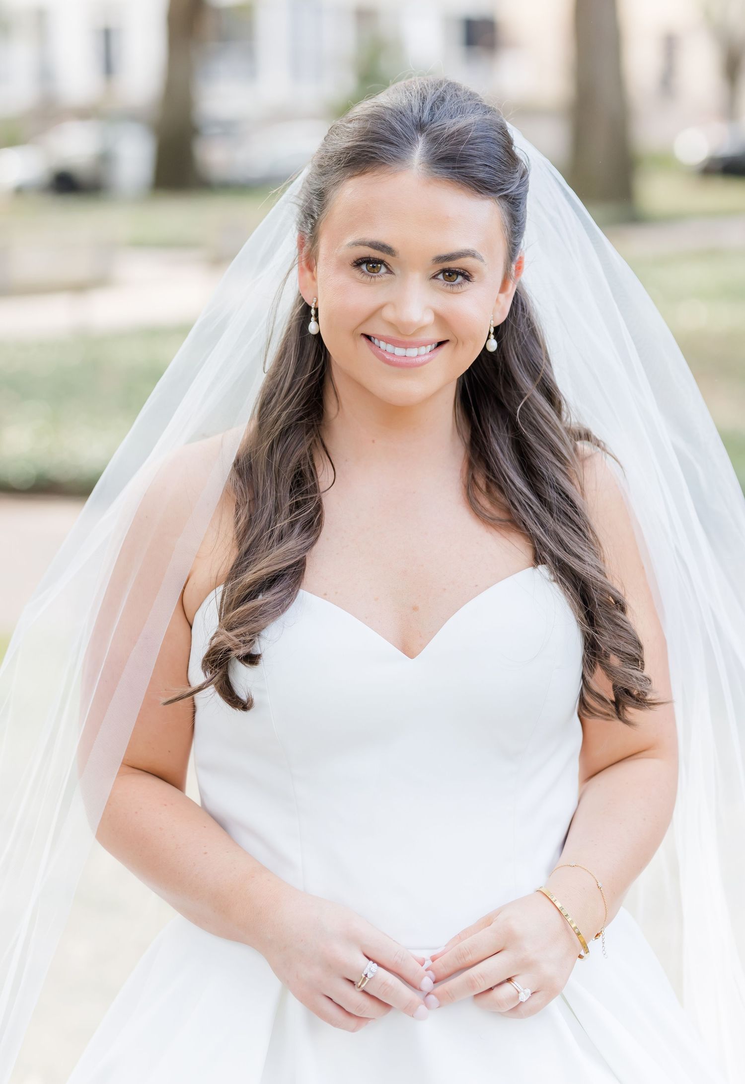 Bride in a classic white wedding dress with a flowing veil poses for bridal portraits outdoors.