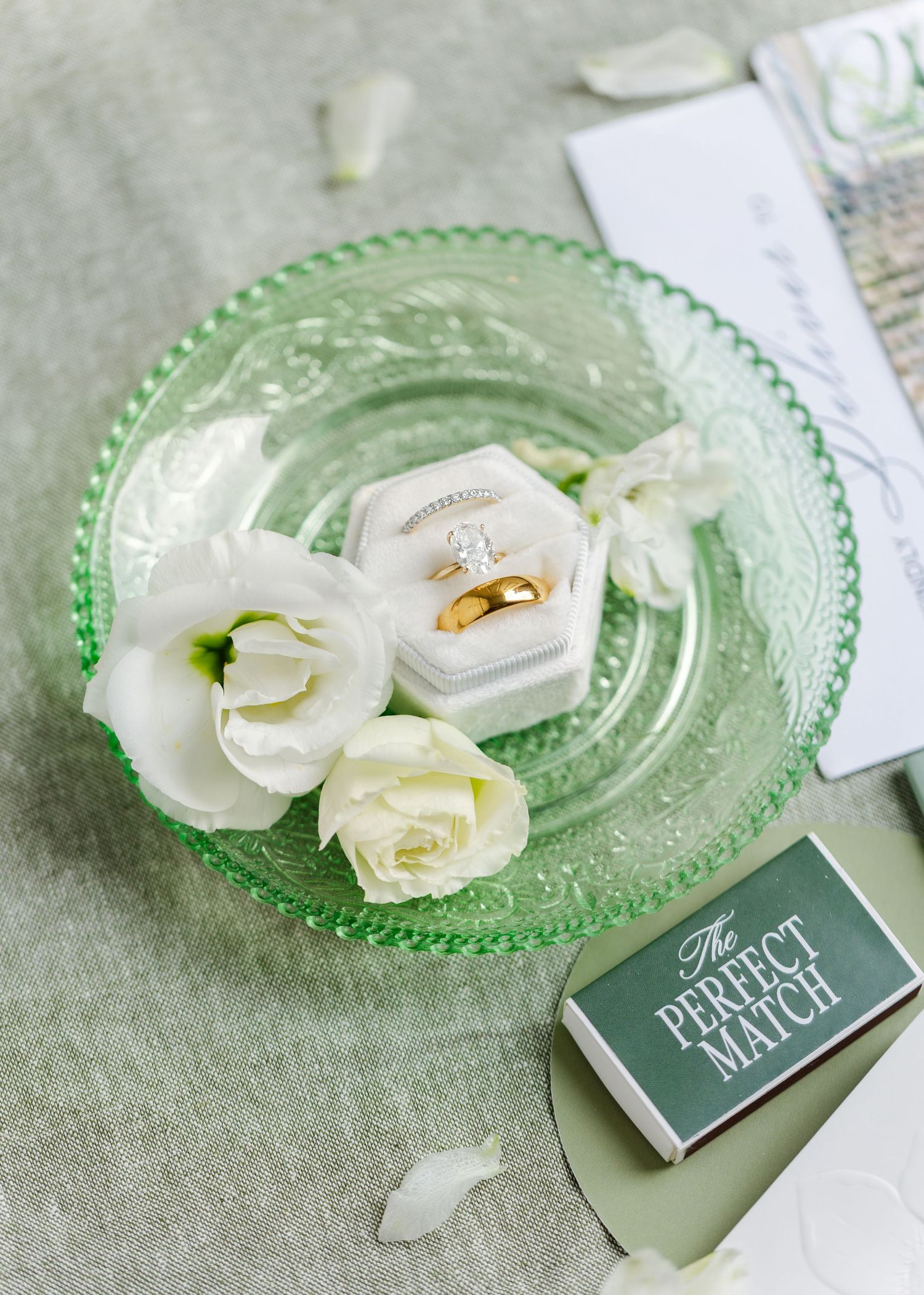 Wedding rings displayed on a mint green glass plate with white roses and a small card.