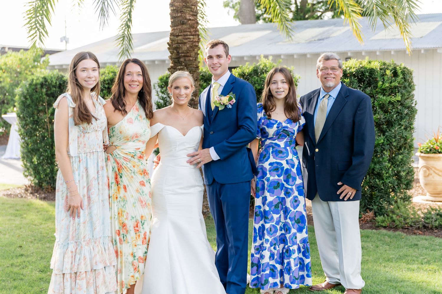 A group in coordinated blue and floral outfits poses together outdoors for a formal summer gathering.
