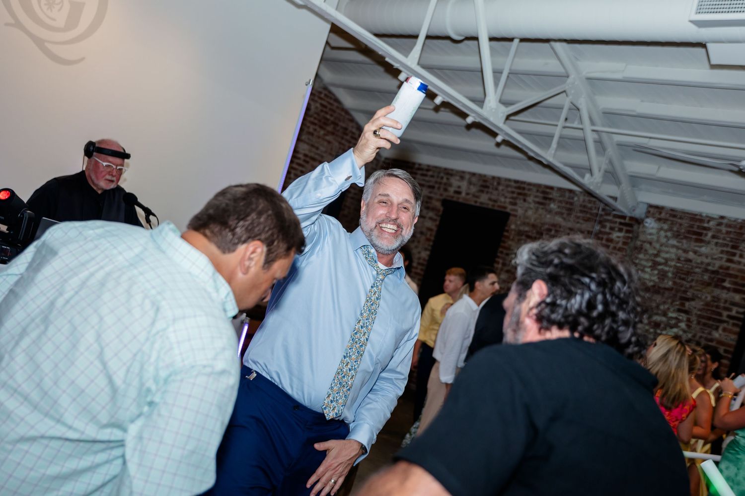 People dancing and celebrating at a lively indoor party or reception with festive lighting and decor.