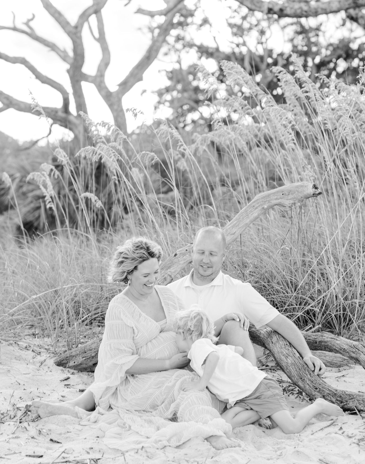 Black and white family portrait on beach with sea grass and natural elements.