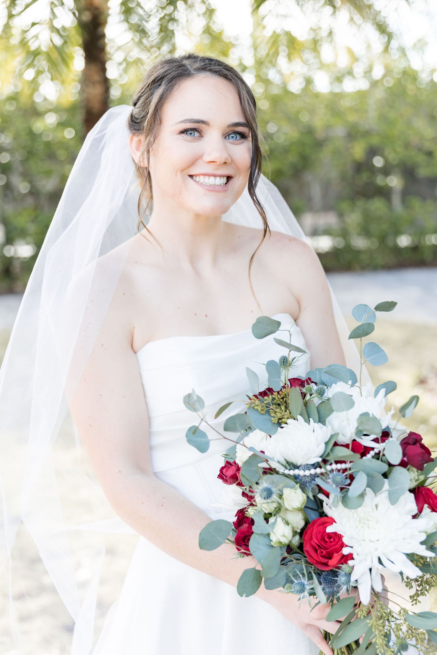 Wedding portraits in natural light featuring a white bridal gown and bouquet with red and white flowers.
