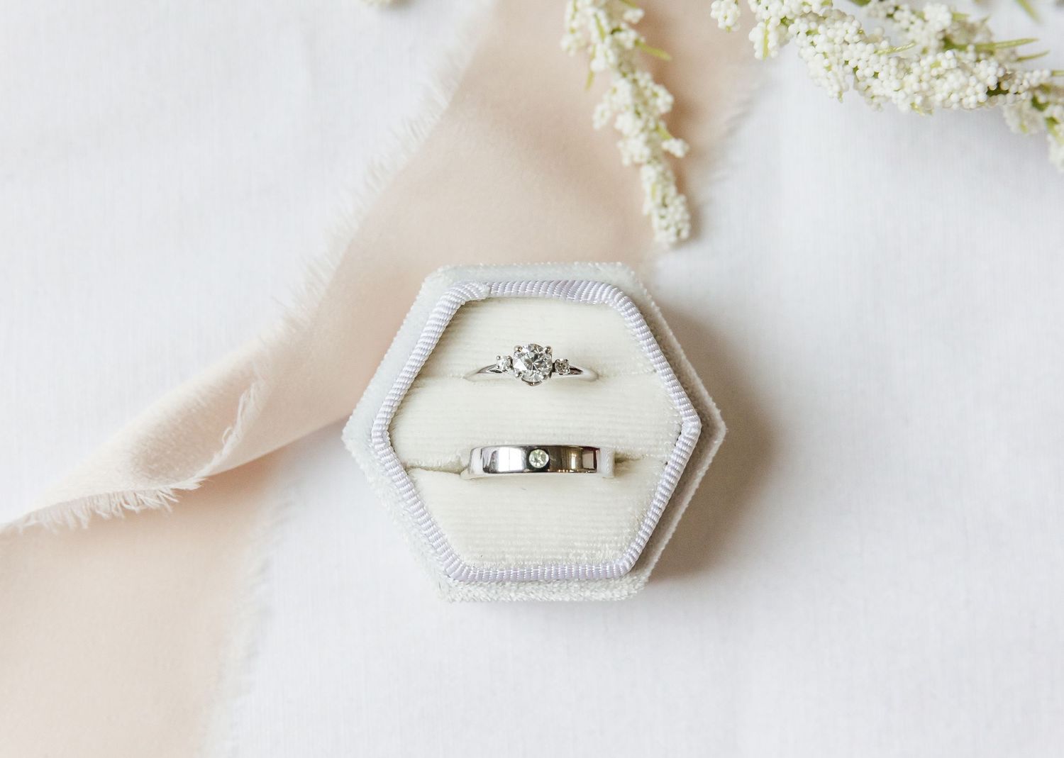 Delicate white hexagonal ring box with lace details on light fabric.