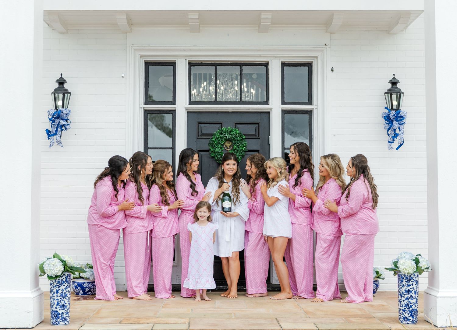 Bride in white robe with bridesmaids in matching pink pajamas posing on front porch steps of a white Southern estate.