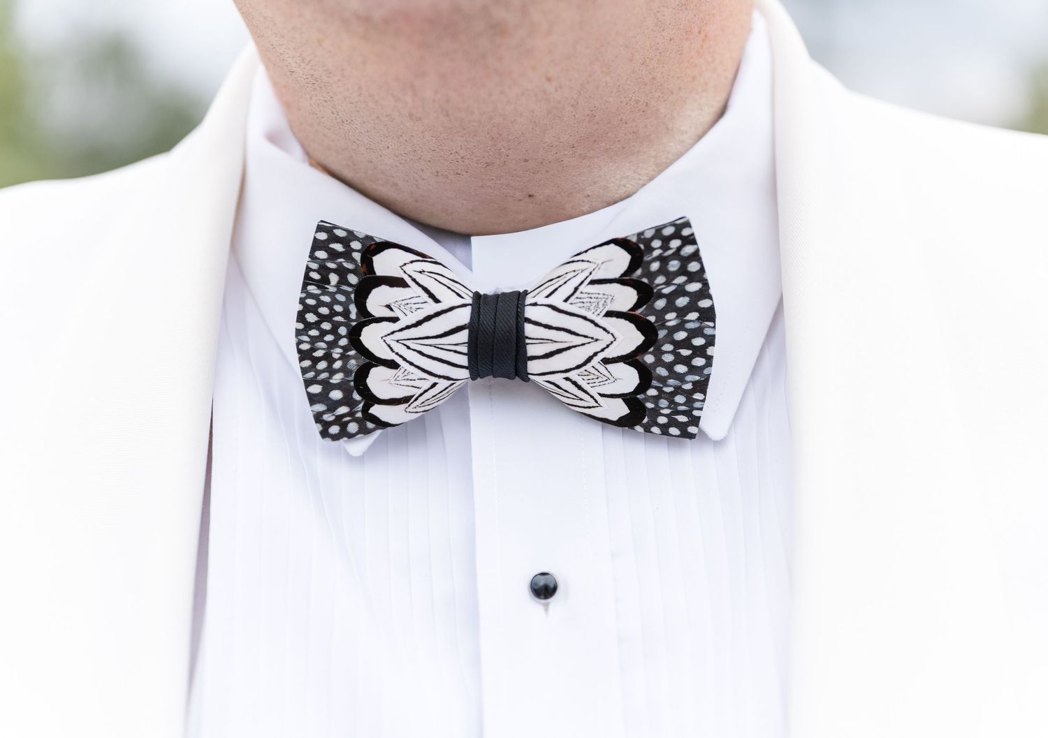 Groom wearing white tuxedo jacket with black and white feather patterned bow tie closeup.
