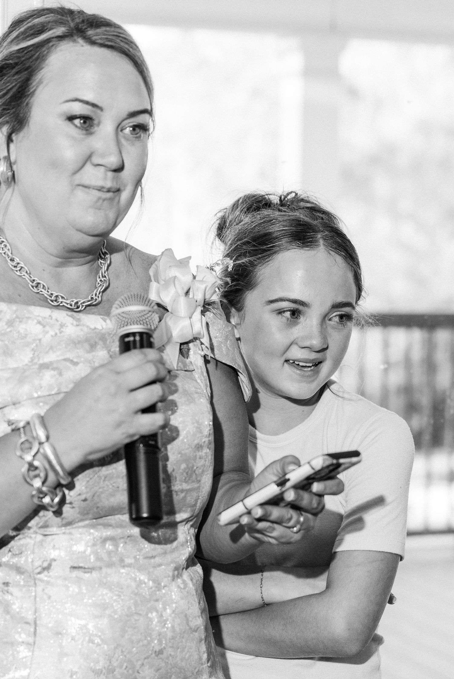 Black and white photo of woman holding microphone giving wedding speech with young girl beside her.