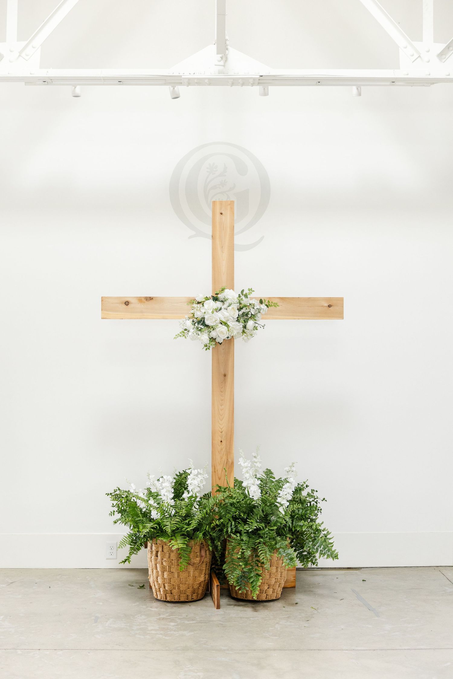 Wooden cross decorated with white flowers and greenery in wicker baskets at a wedding ceremony.