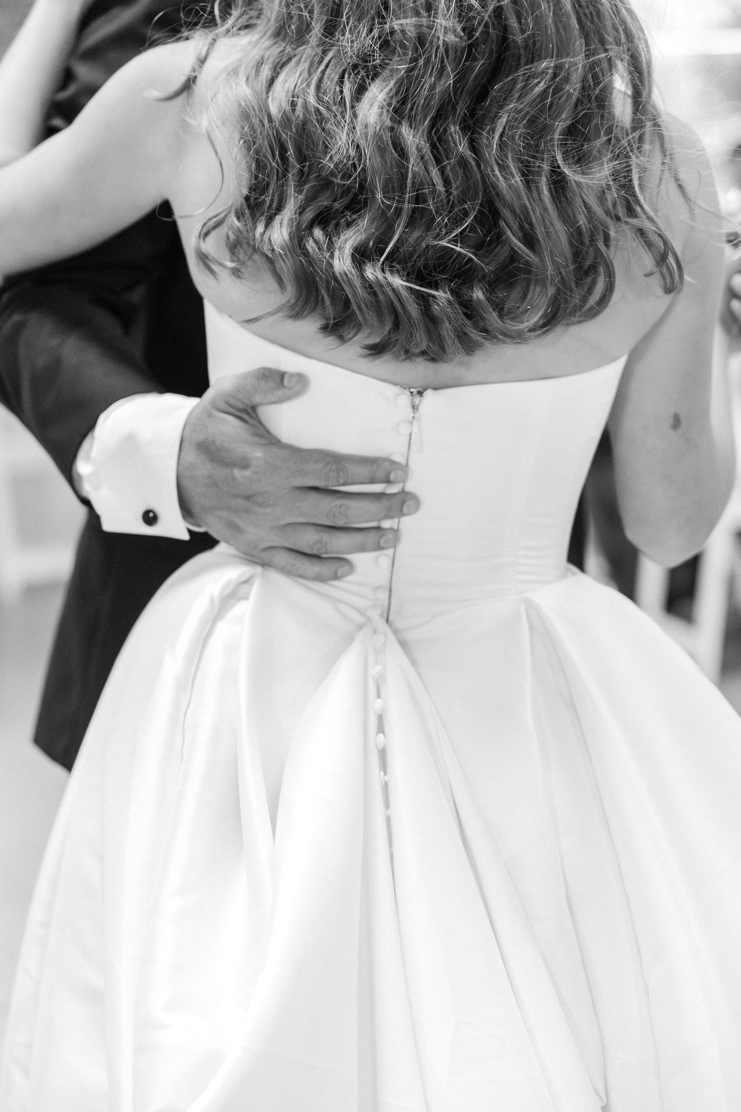 Black and white close-up of groom's hand on bride's white satin wedding gown back.