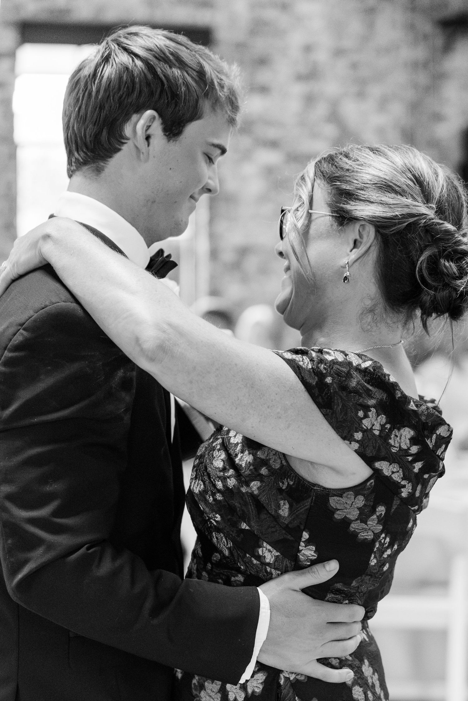 Groom shares tender mother-son dance moment in black and white photo at wedding reception.
