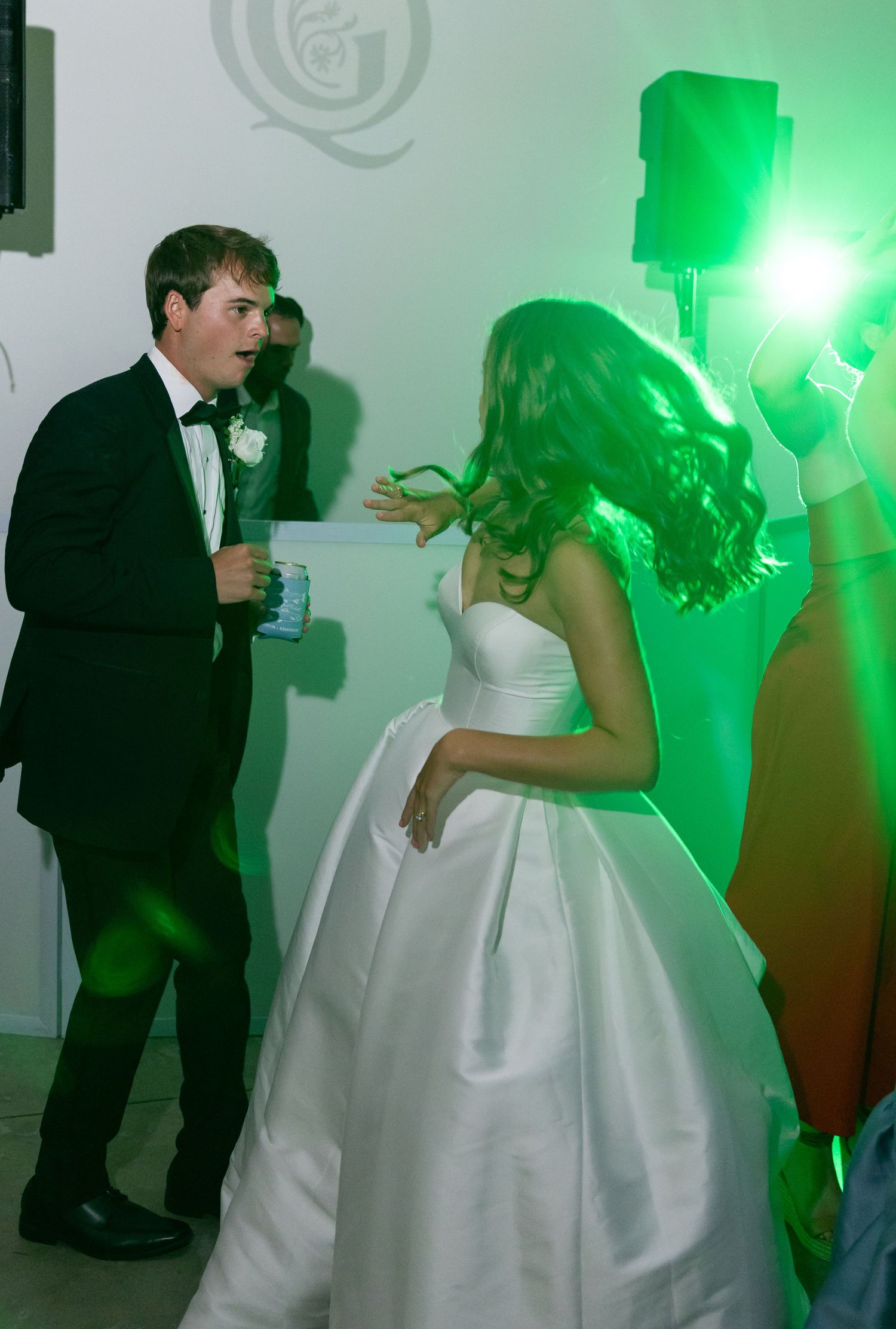 Bride and groom dance under dramatic green lighting during their lively wedding reception celebration.