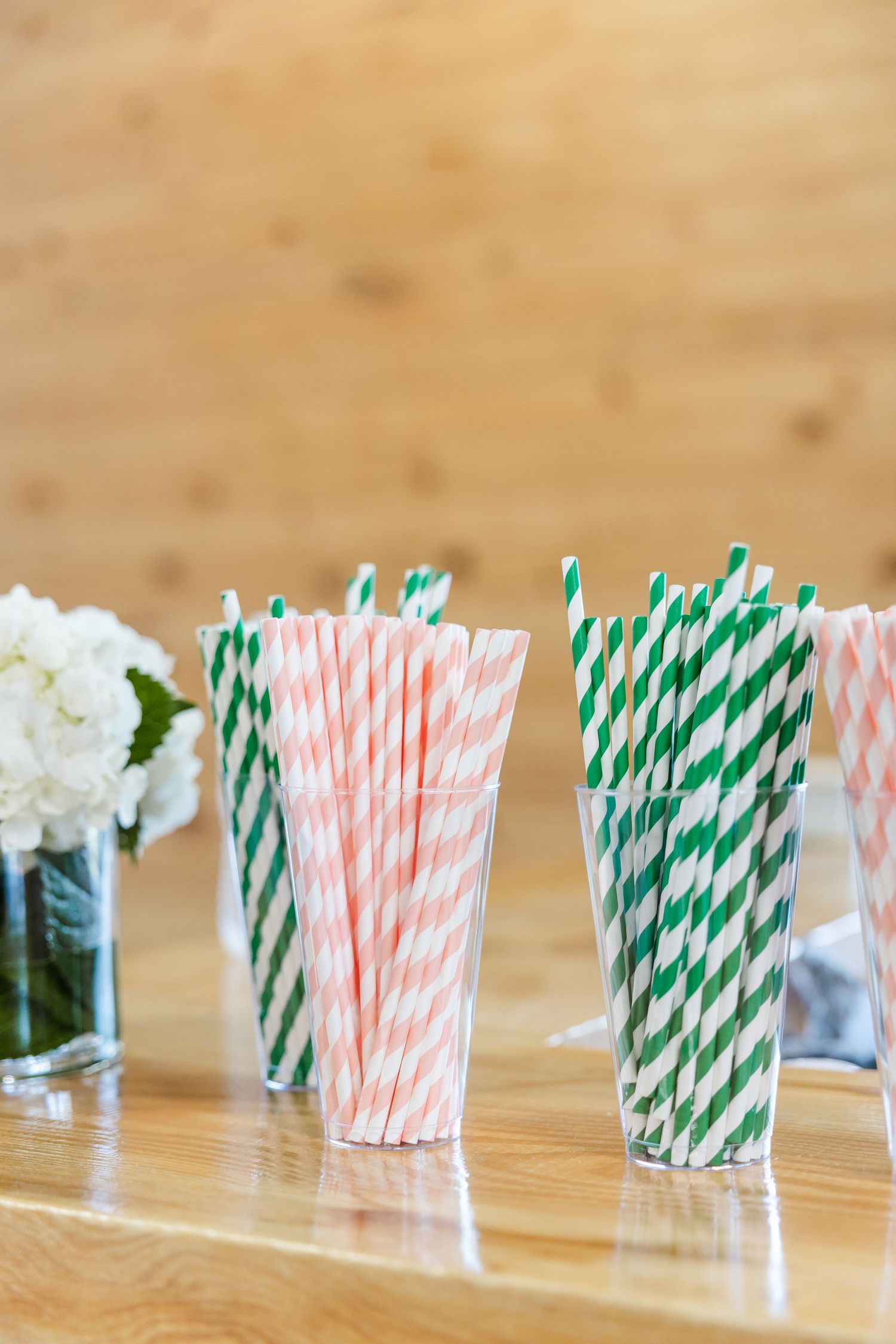 Pink and green striped paper straws displayed in clear glasses on a wooden table at a wedding reception.