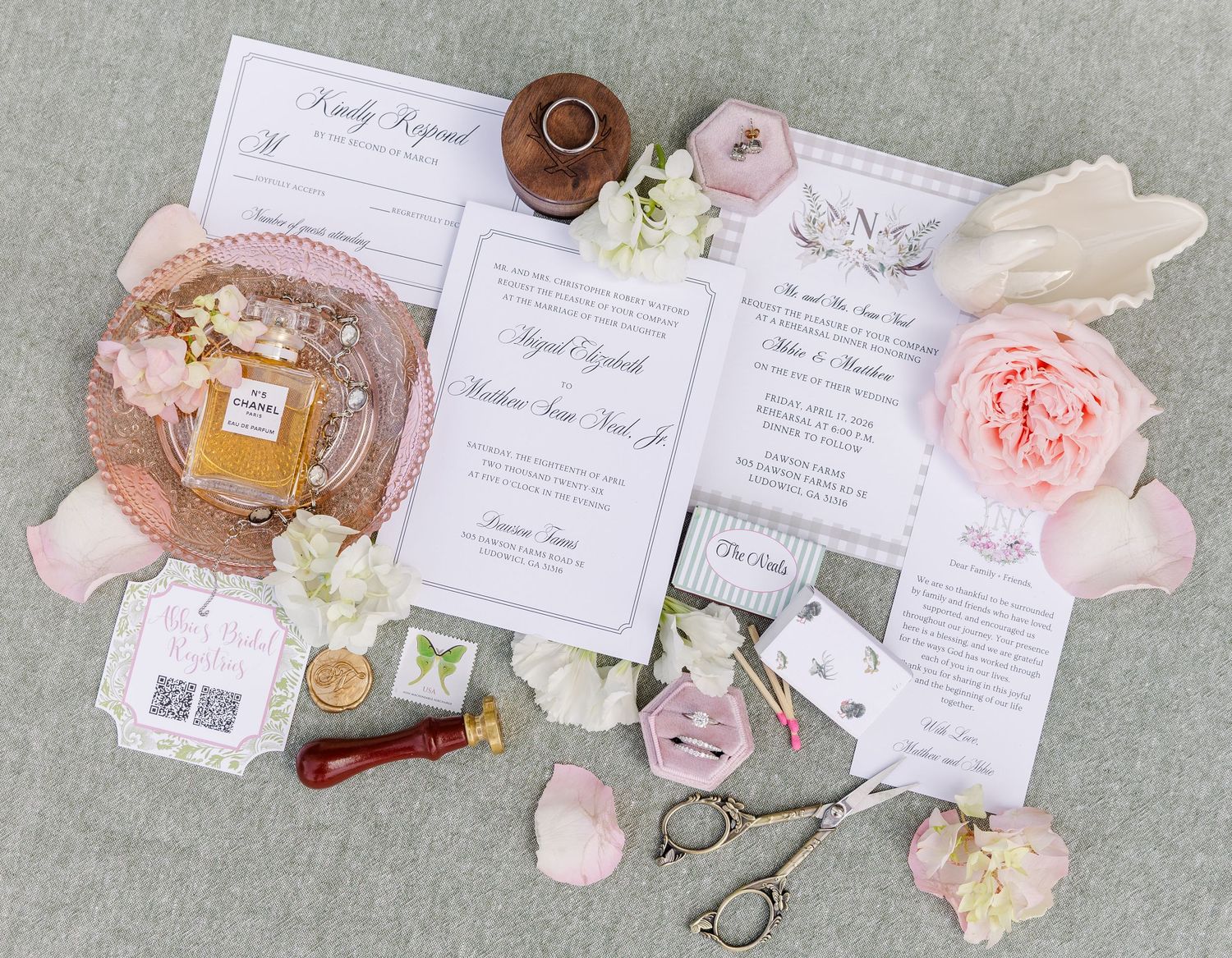 Elegant wedding invitation suite with pink roses, Chanel perfume, wax seal, scissors, and floral stationery on gray background.