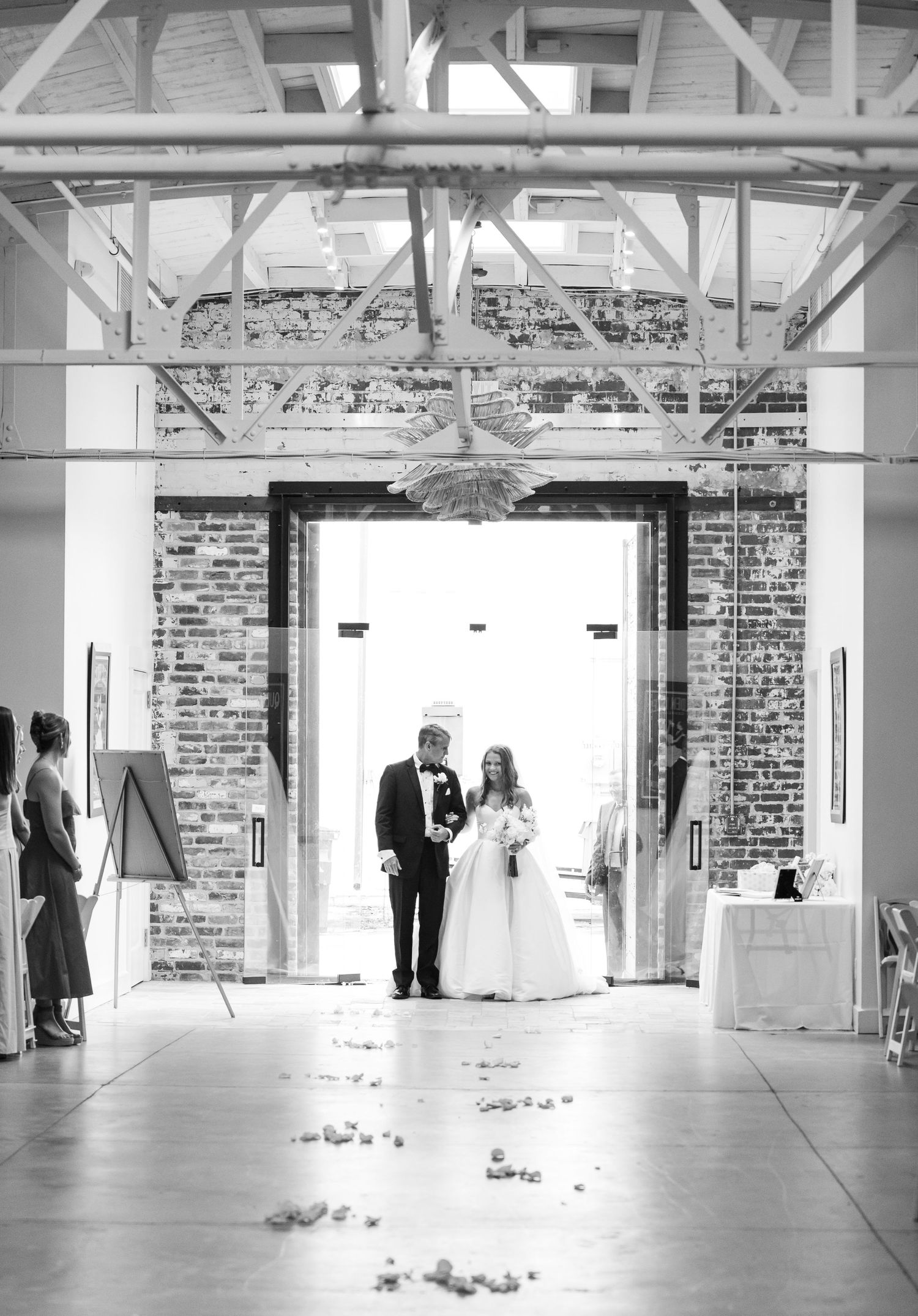 Black and white photo of bride and groom entering wedding ceremony through grand brick archway in rustic venue.