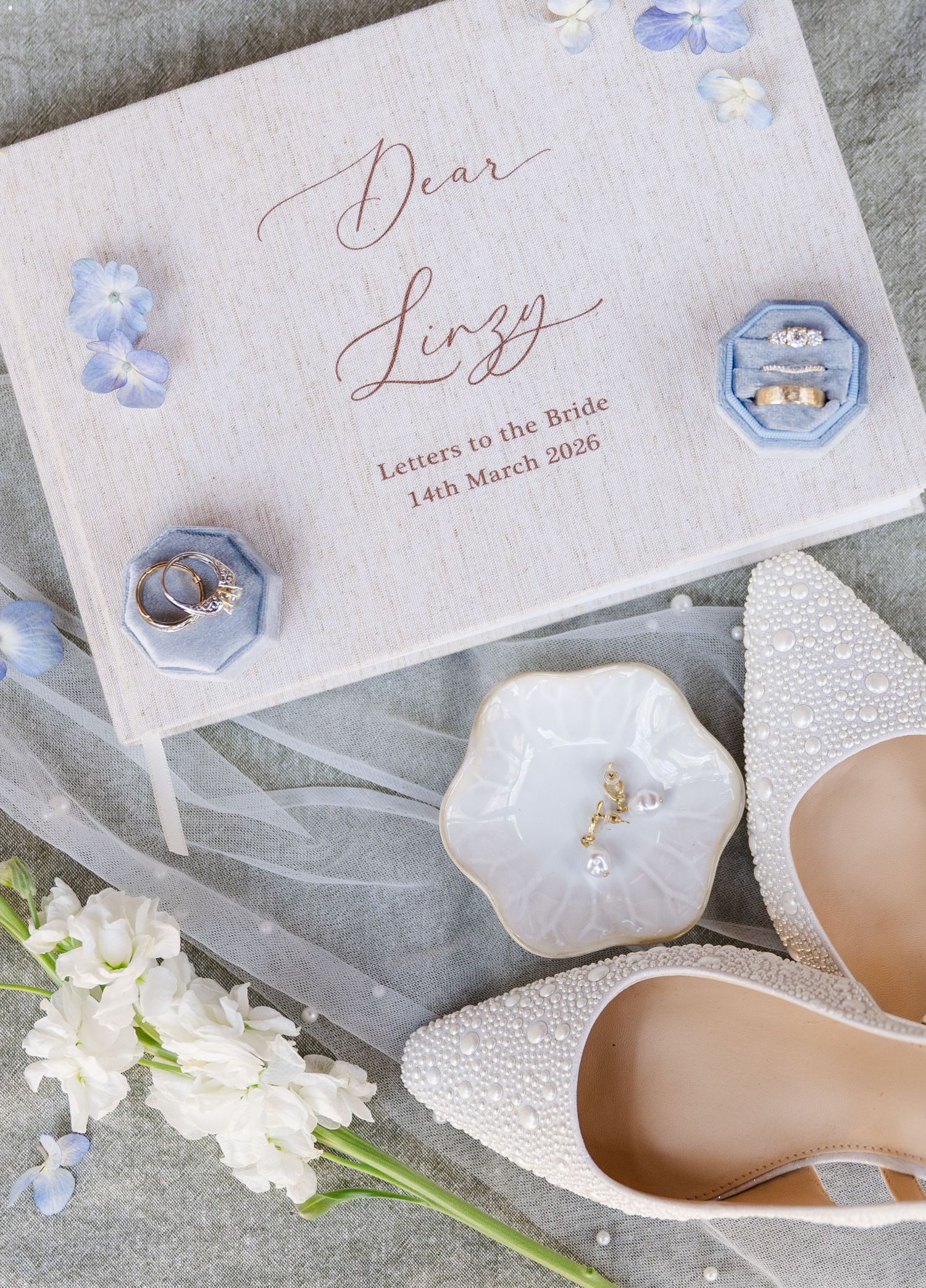 Elegant wedding flat lay with pearl heels, blue ring boxes, floral details, and a personalized Dear Bride letter box dated March 2026.