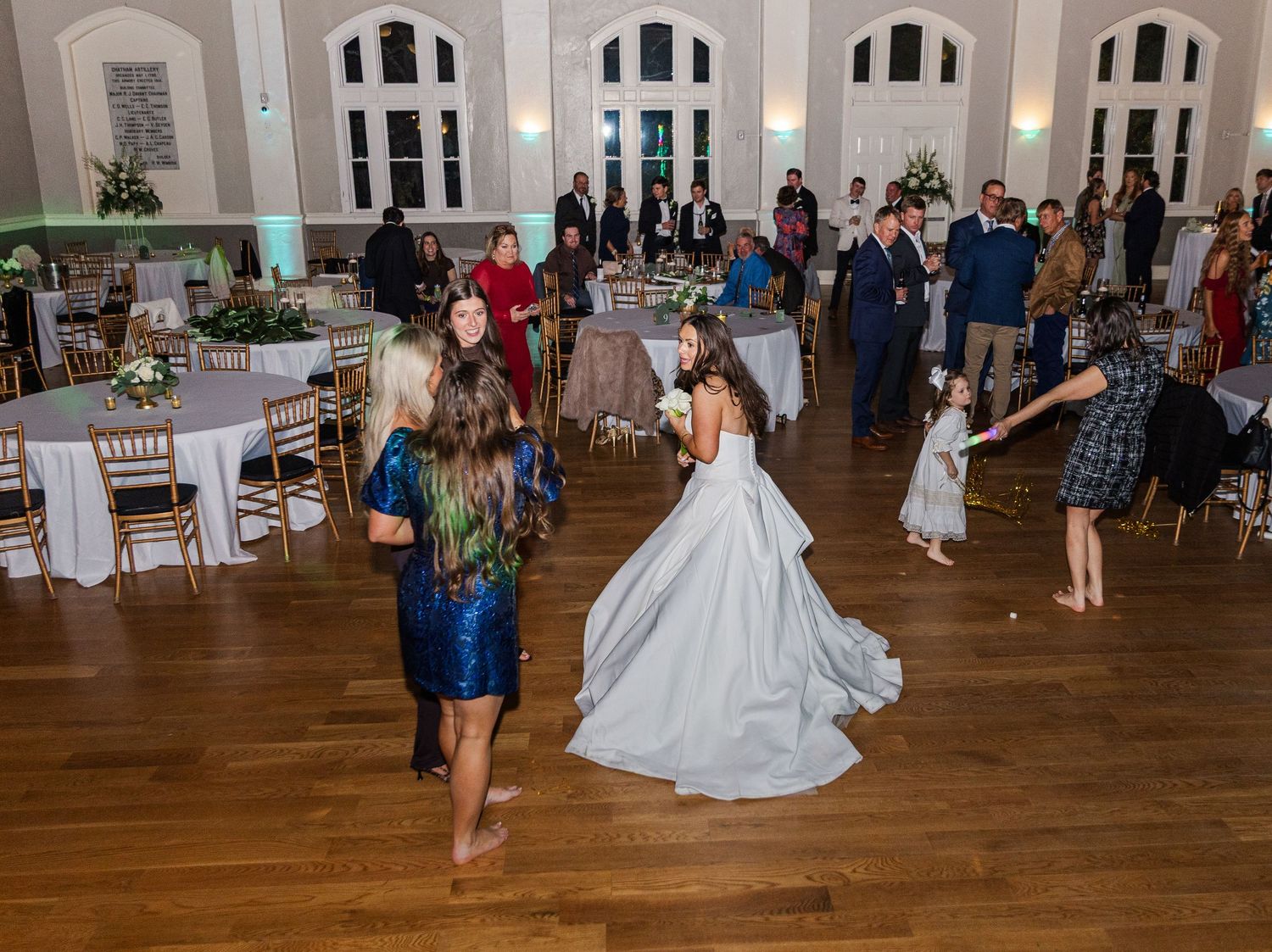 Bride in white gown dances with guests on the hardwood floor of an elegant wedding venue.