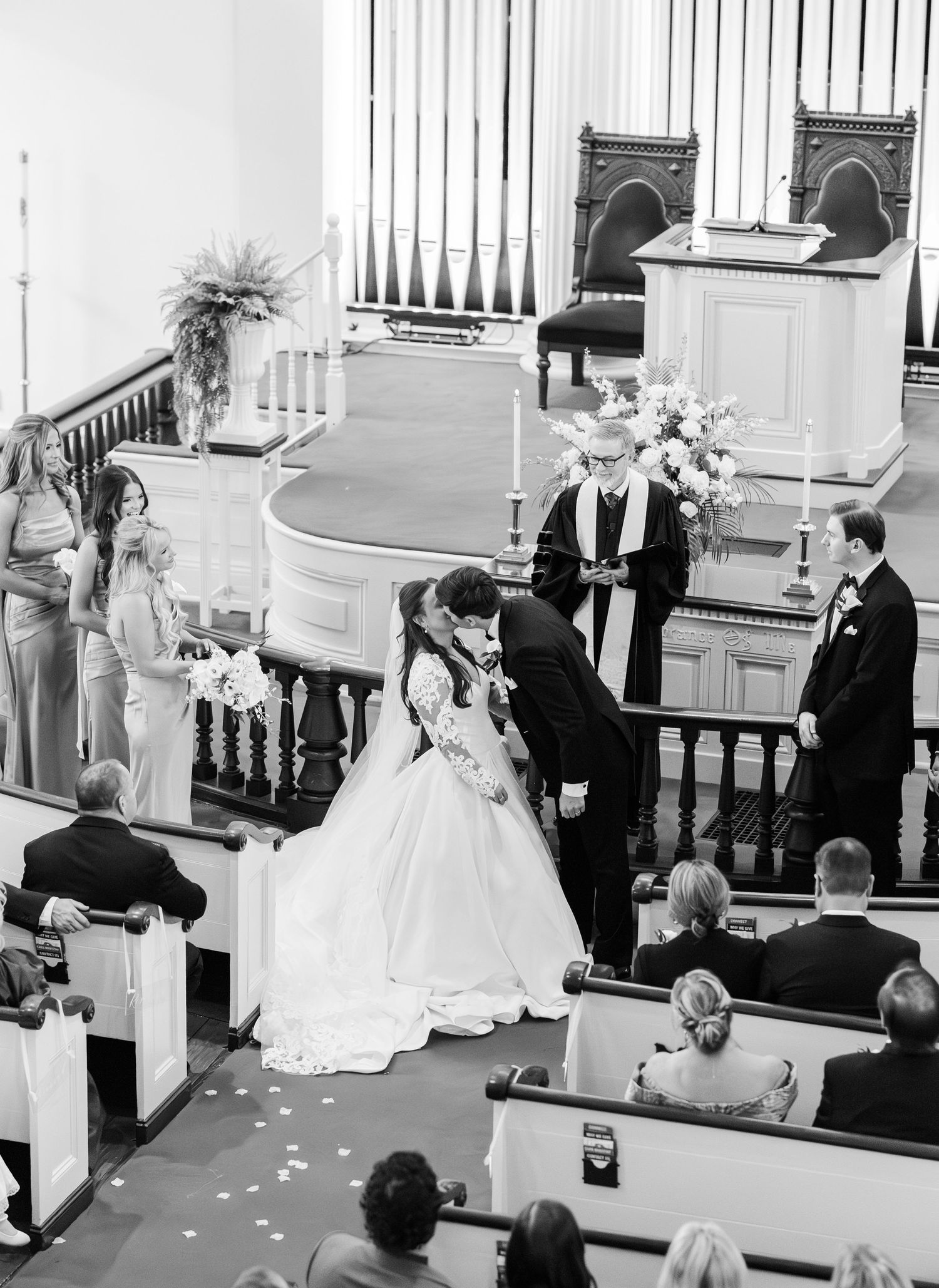 Black and white photo of bride and groom kissing at church altar during wedding ceremony.