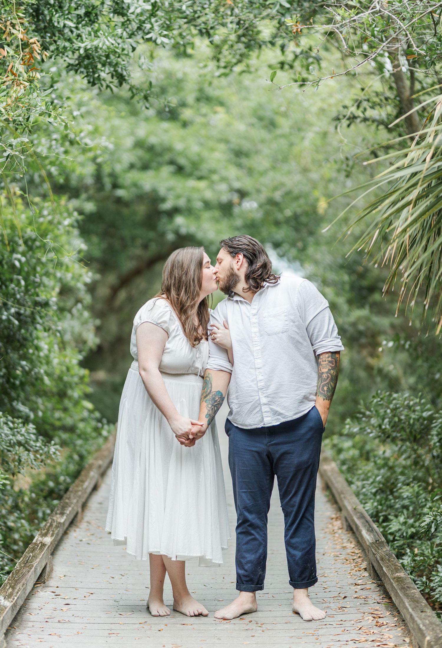 A couple shares a tender moment on a wooden walkway surrounded by lush greenery.