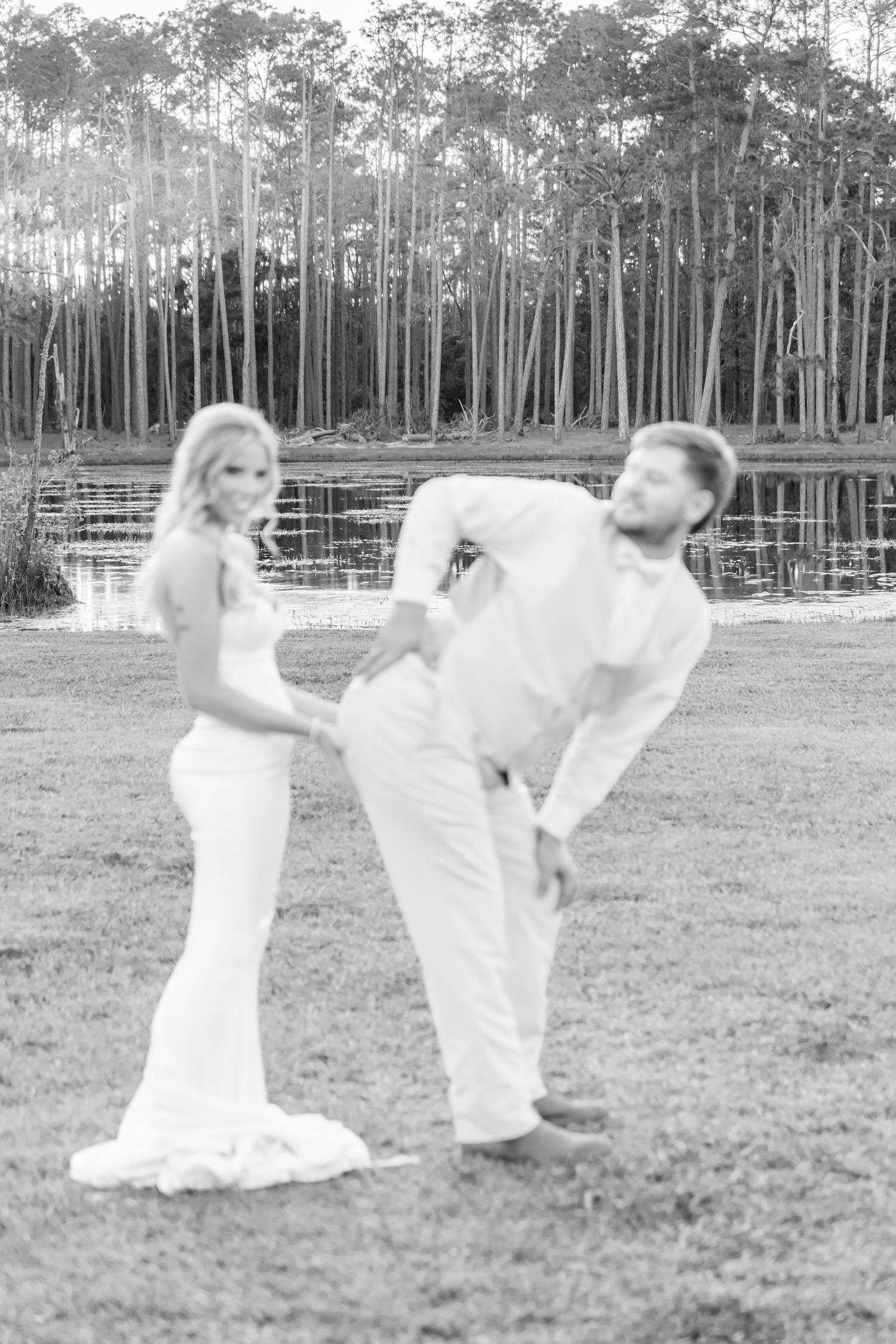 Candid black and white wedding photo capturing couple's playful moment by the lake.
