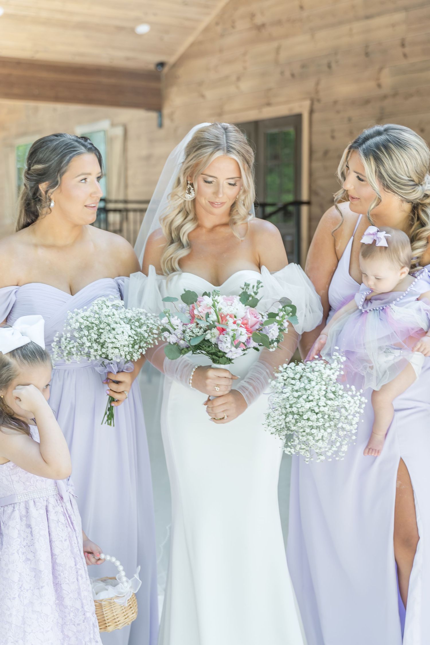 Intimate moment between bridal party members holding bouquets outside rustic venue.