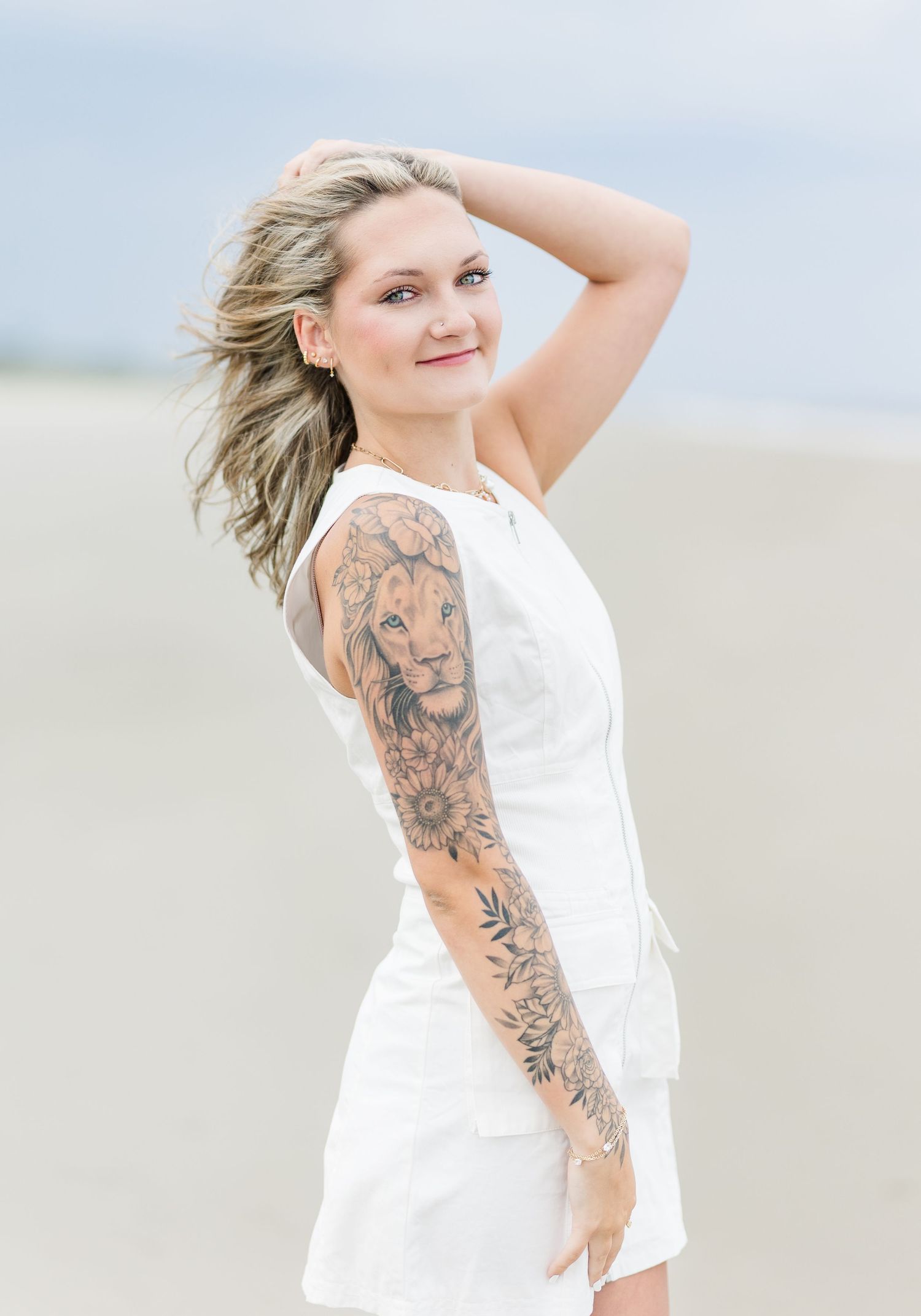 Windswept beach photo with white dress and detailed lion sleeve tattoo against soft lighting.