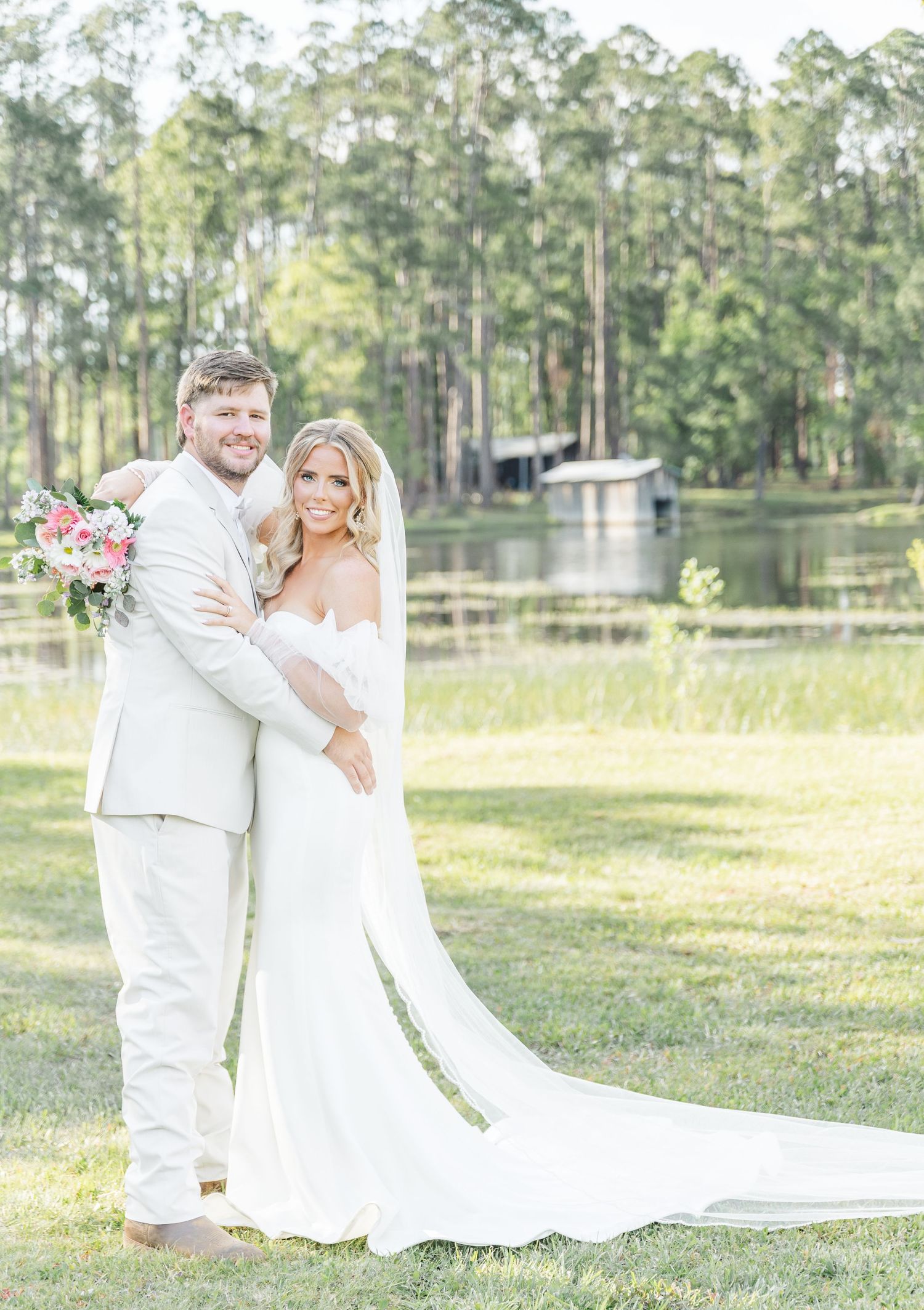 A classic wedding portrait of a couple in all white against a scenic lake and pine forest backdrop.