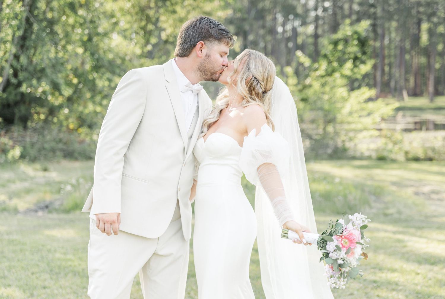 Intimate moment between newlyweds in white against a soft, ethereal forest backdrop.