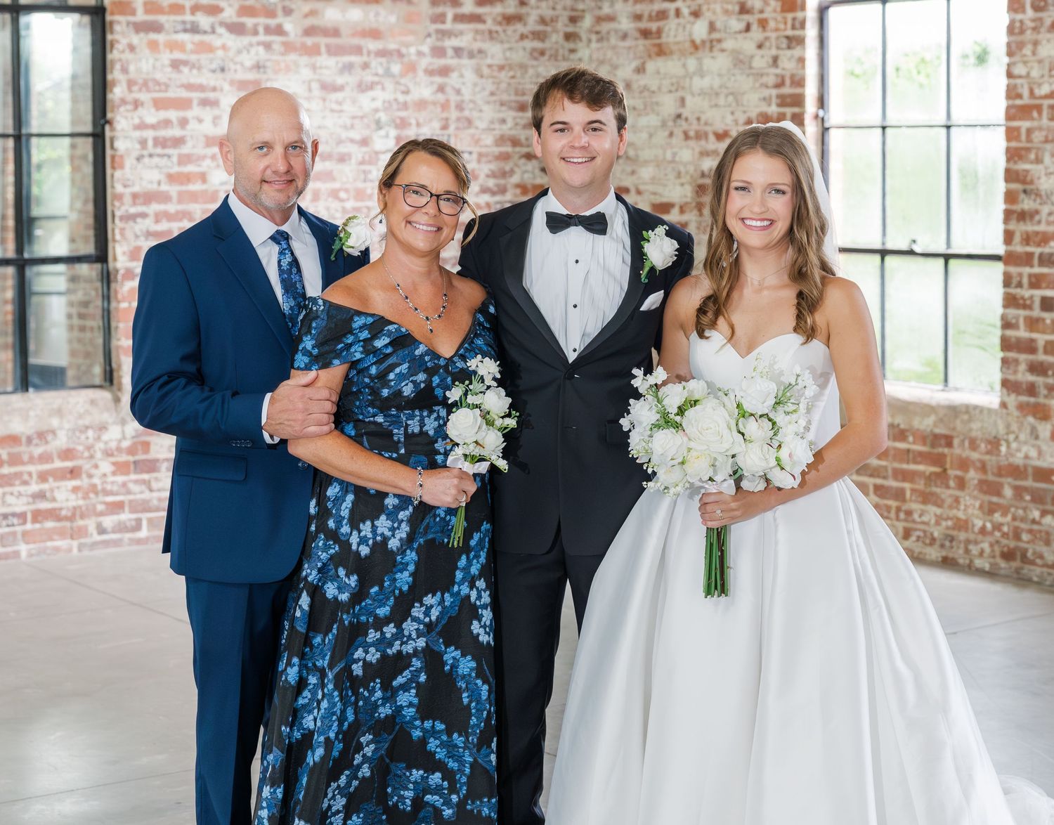 Bride and groom pose with family in elegant brick venue, bride holding white bouquet in strapless ball gown.