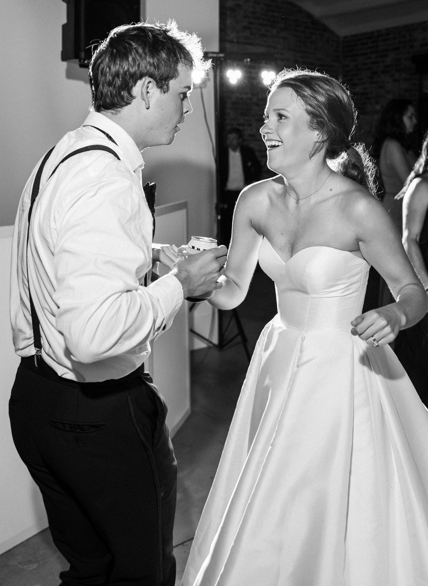 Black and white photo of bride and guest sharing joyful dance moment at wedding reception.