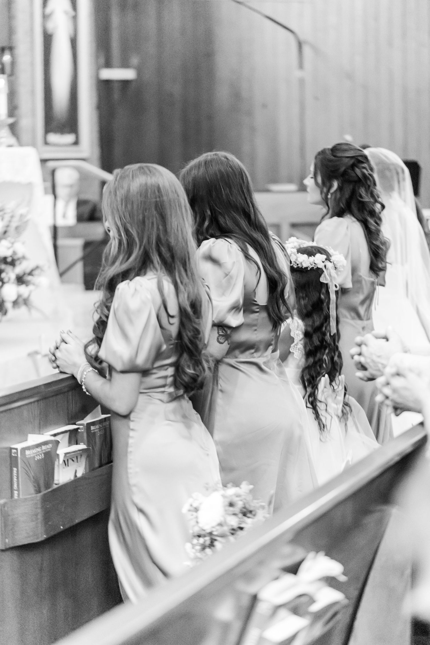 A black and white photo of bridesmaids in light dresses standing at a church altar.