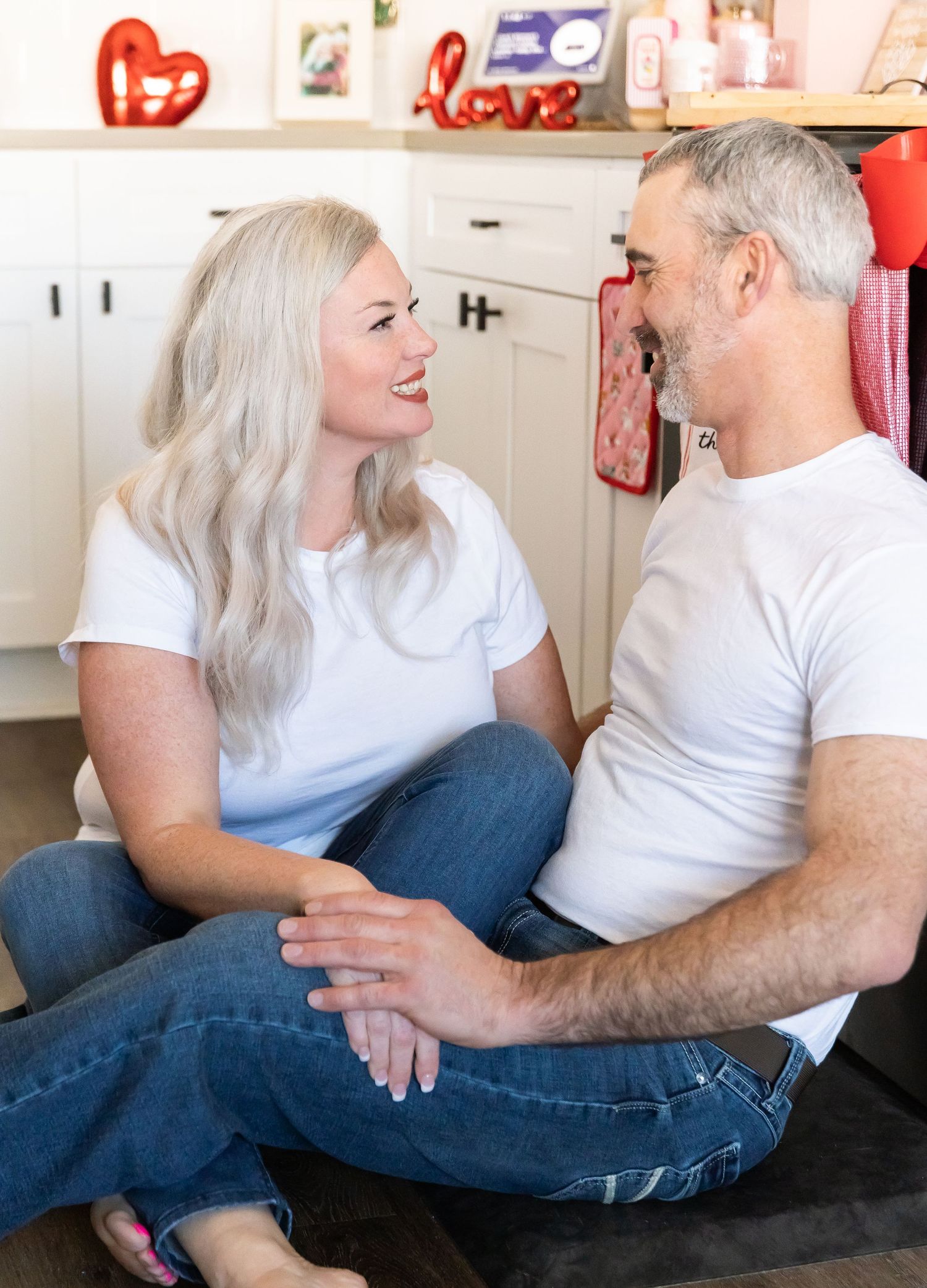 A couple shares a joyful moment while sitting together in their kitchen with Valentine's decorations.