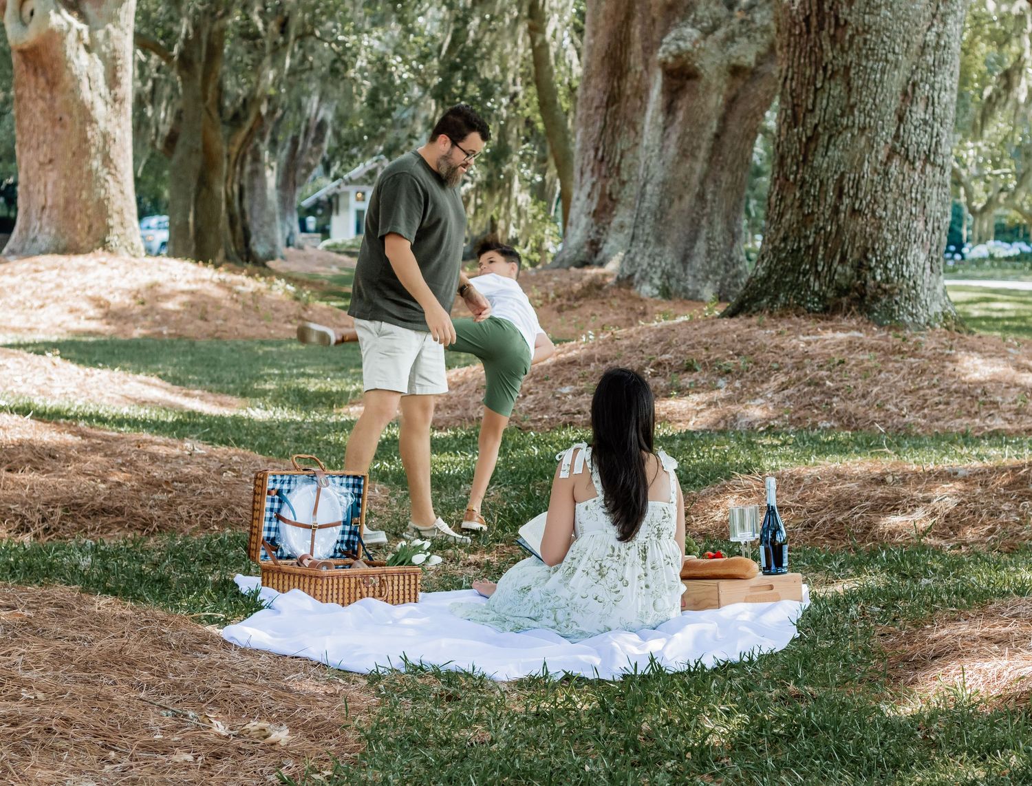 Family members dance and play during a sunny afternoon picnic under oak trees.
