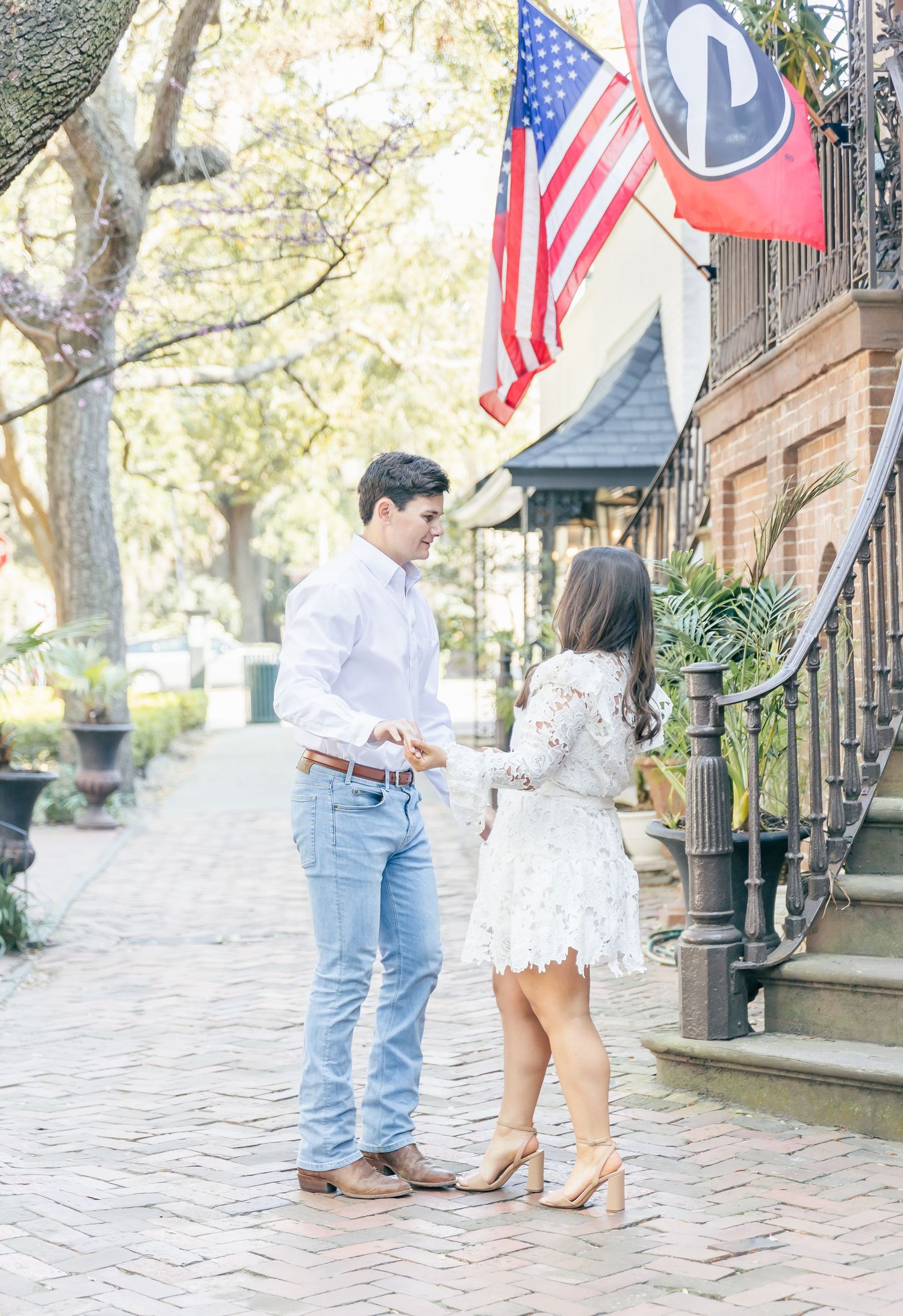 A couple stands together on a brick sidewalk with an American flag and red banner displayed above them.